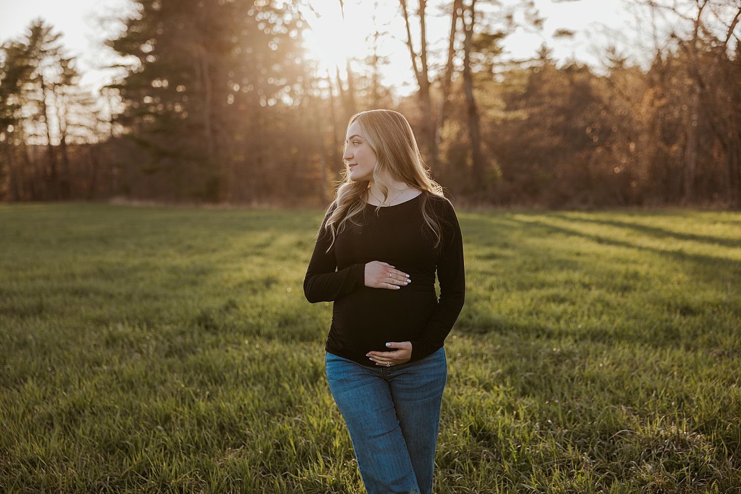 Woman posing for maternity photos in a fall field in New Hampshire during golden hour