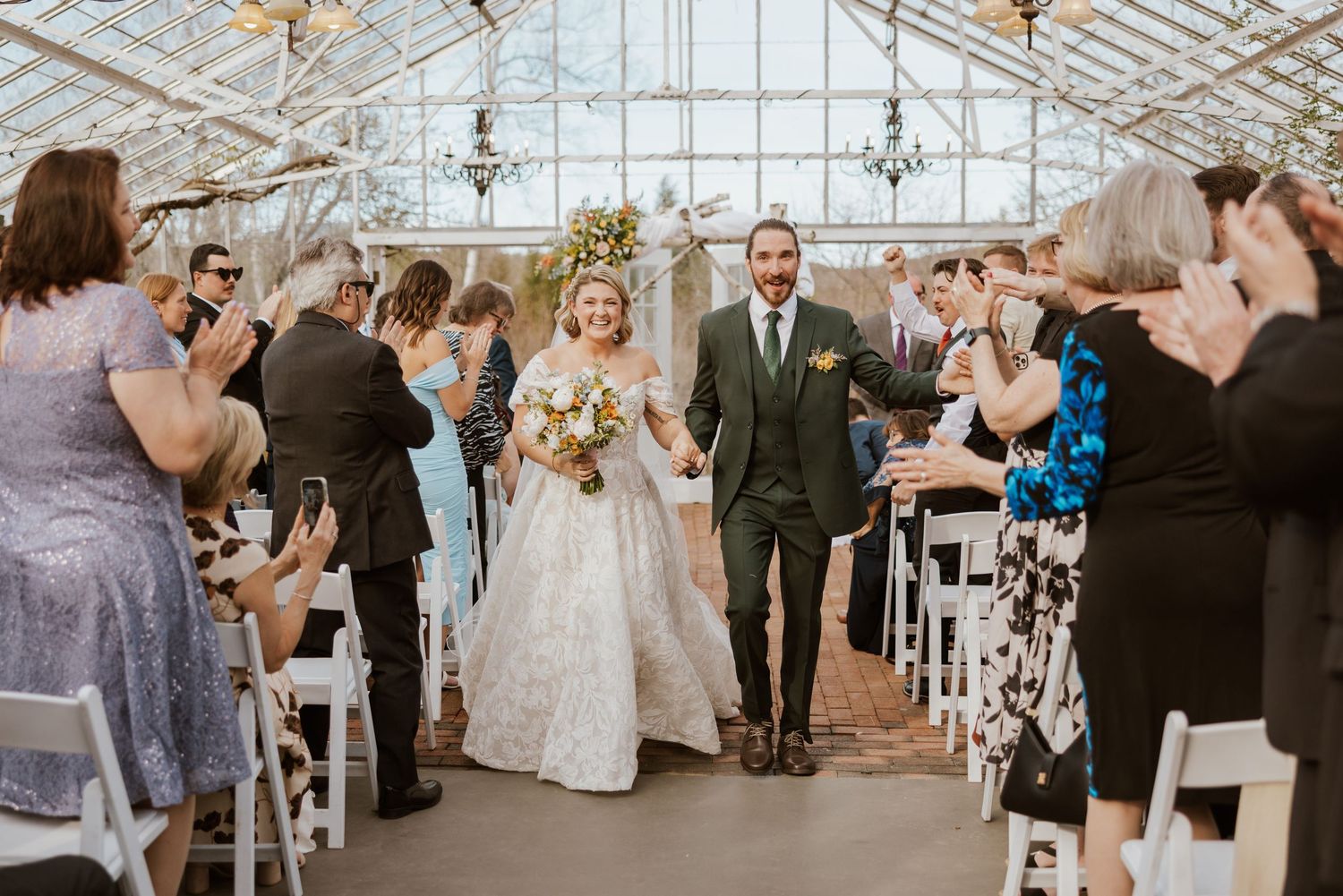 Bride and groom walk hand-in-hand down the aisle in a beautiful glass greenhouse wedding ceremony.