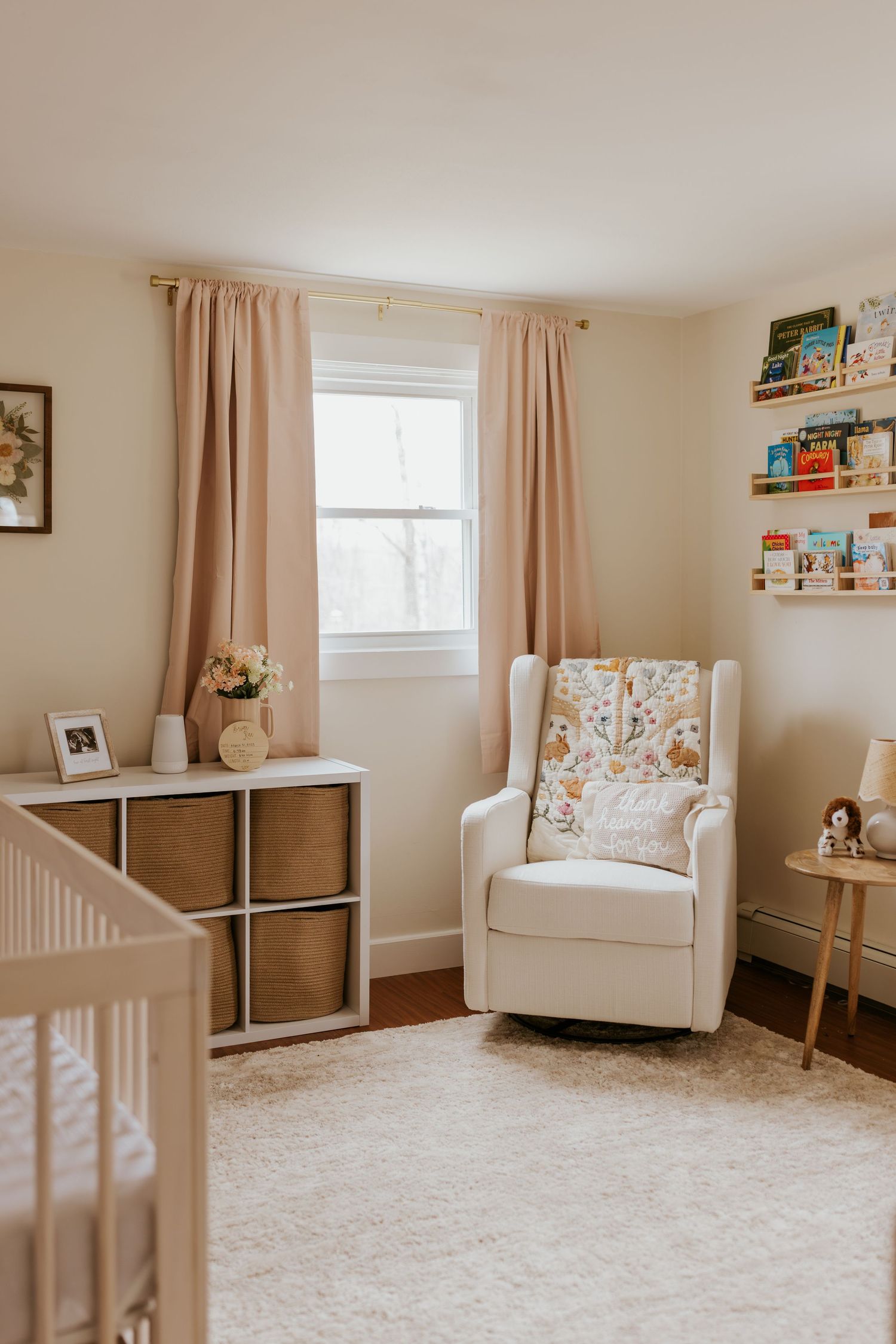 Soft neutral nursery room with white glider chair, crib, and floating bookshelves.