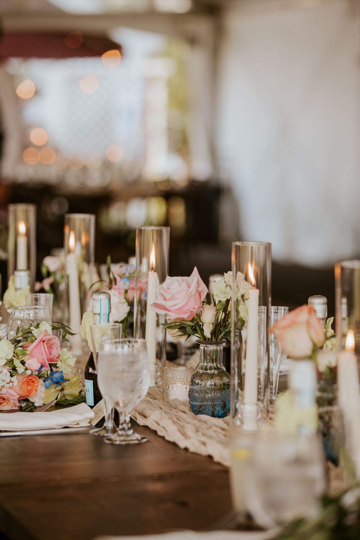 Romantic wedding reception table with pink roses, candles, and glassware on wooden table.