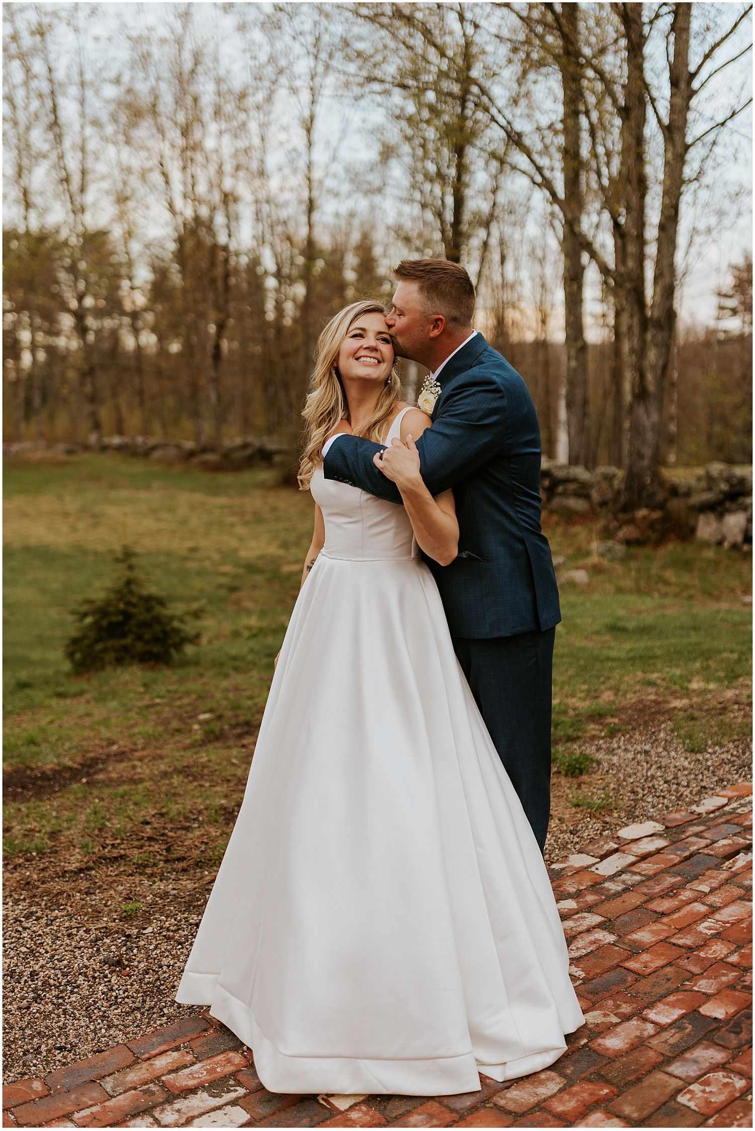 A couple shares a romantic moment on a brick pathway surrounded by autumn trees.