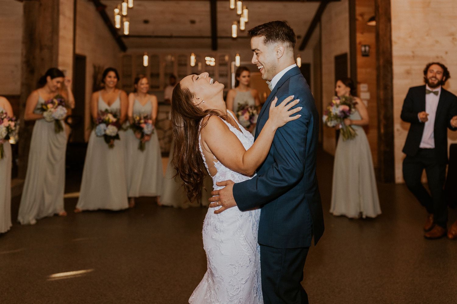 Couple embraces during their wedding dance in a beautifully lit barn venue.