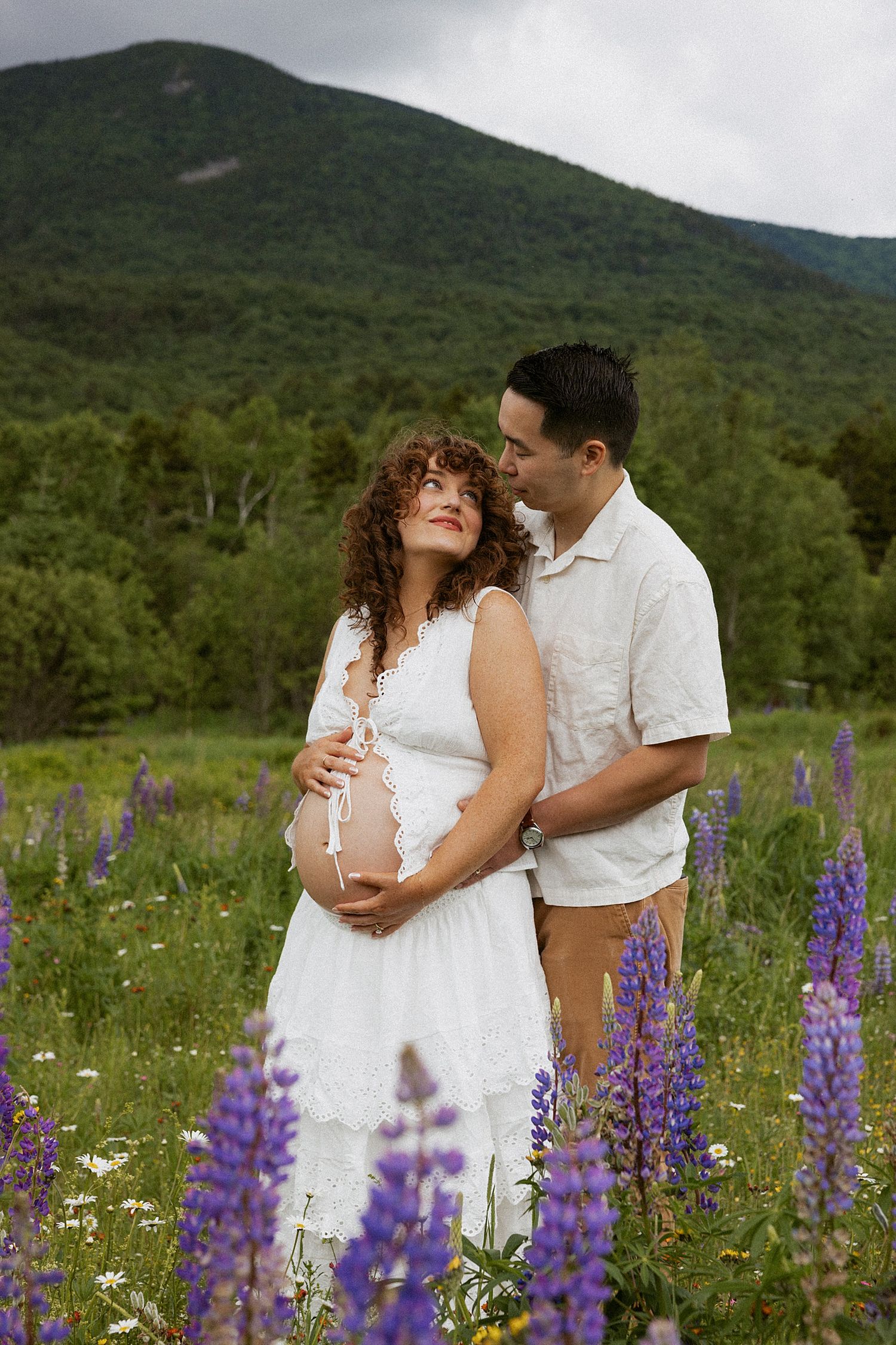 Pregnant woman in white dress with partner in a wildflower field in NH taking motherhood photos