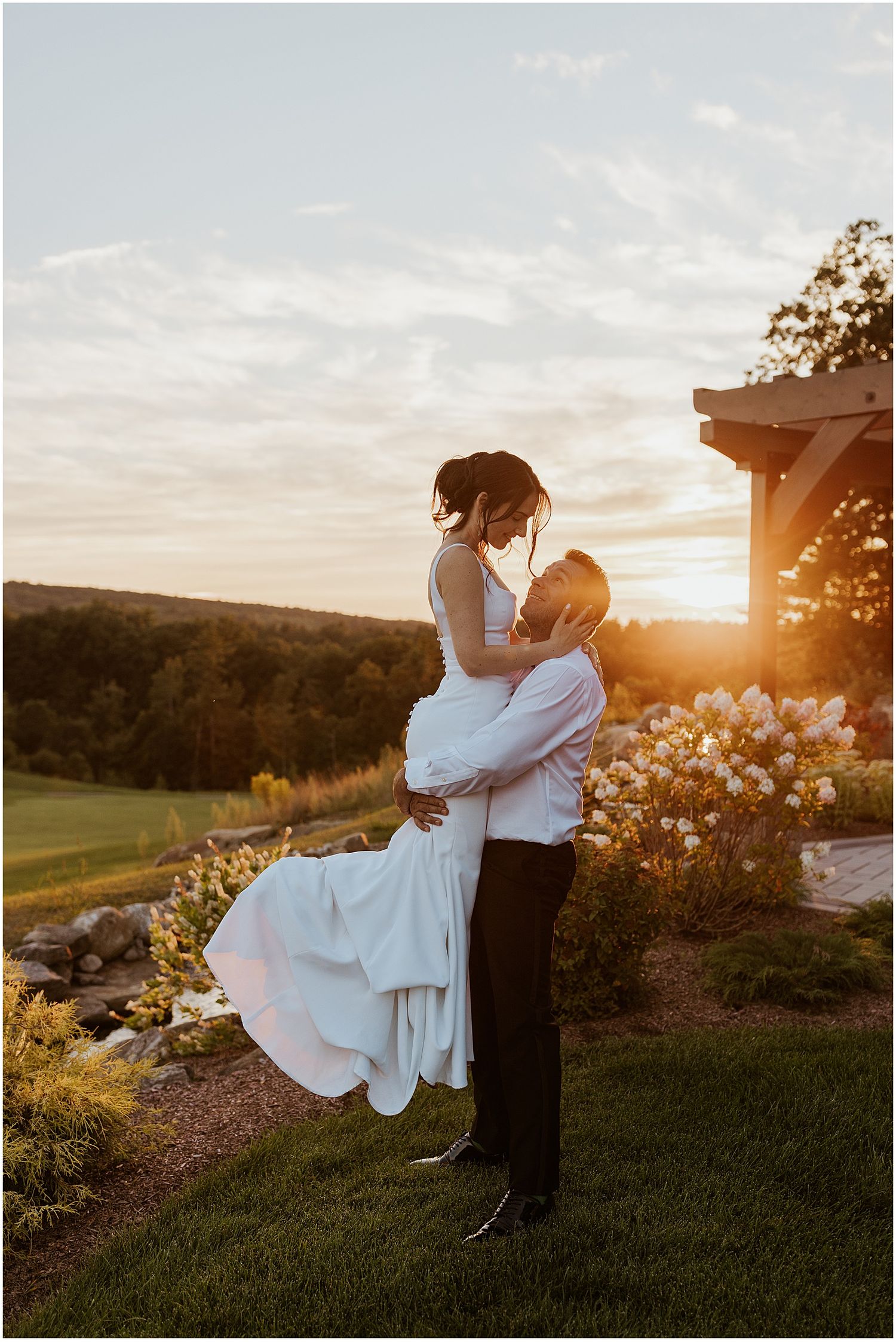 Couple in formal attire sharing romantic sunset moments on a hilltop garden.