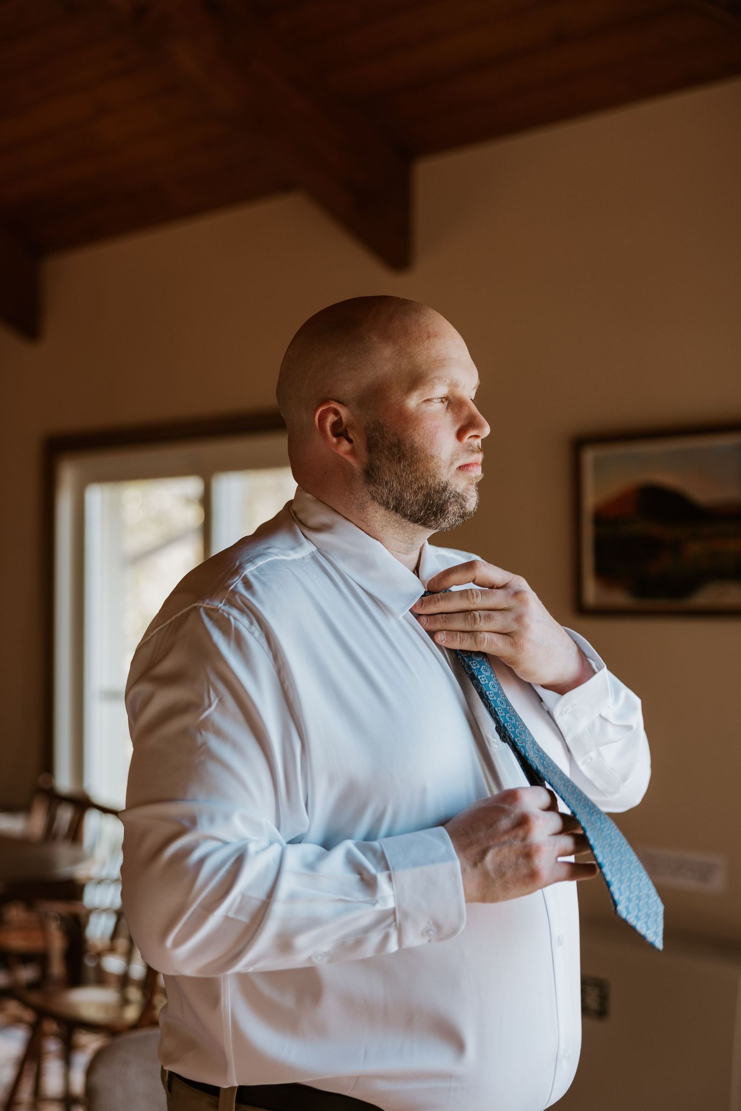 A person in a white dress shirt and blue tie adjusts their collar while getting dressed.
