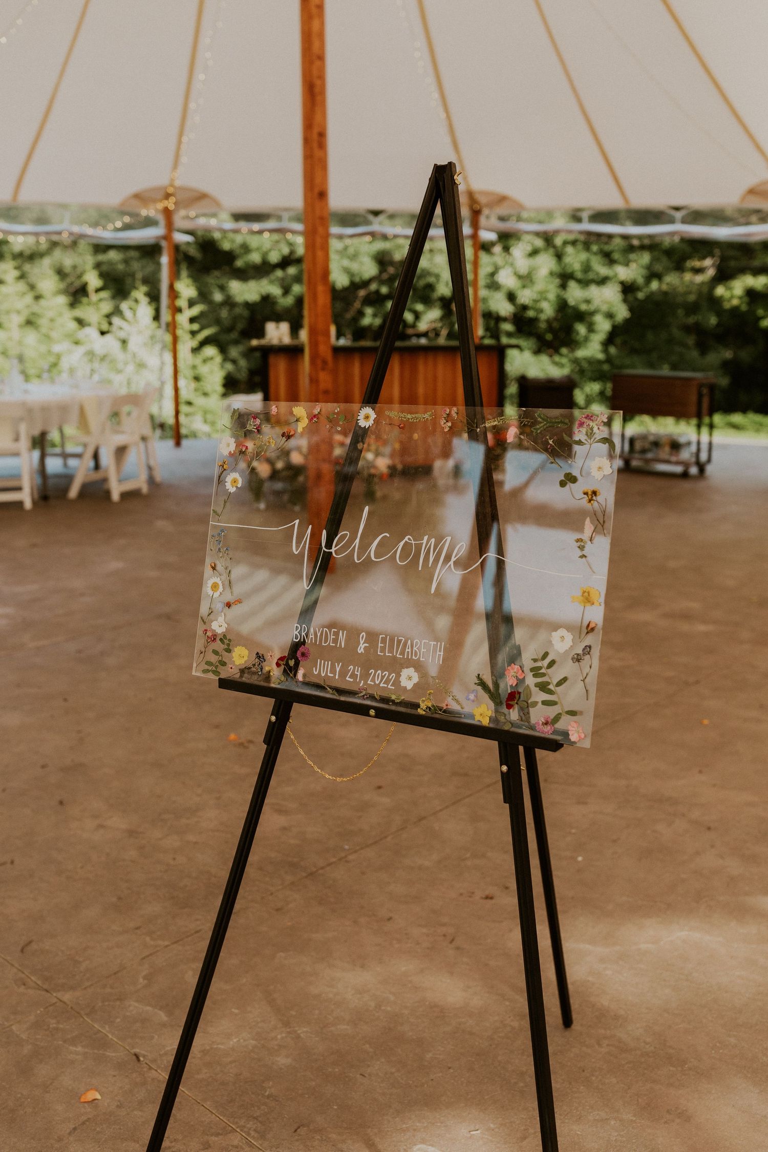 Rustic wooden welcome signs displayed on easels at an outdoor wedding venue.