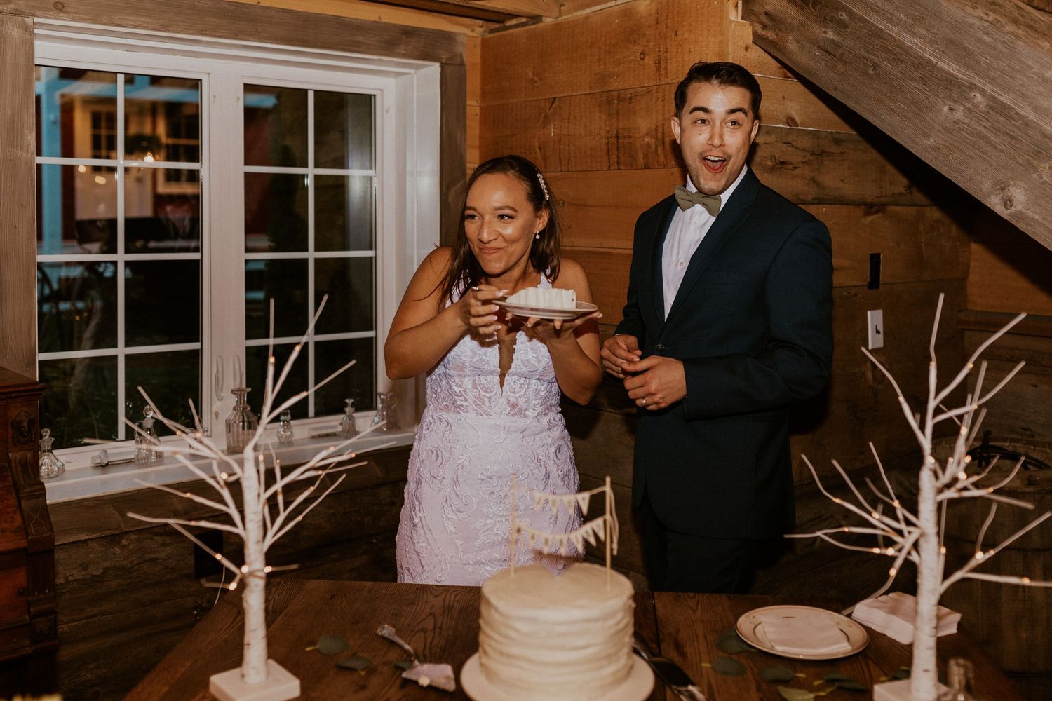 Newlyweds participating in traditional cake cutting ceremony at rustic wedding venue.