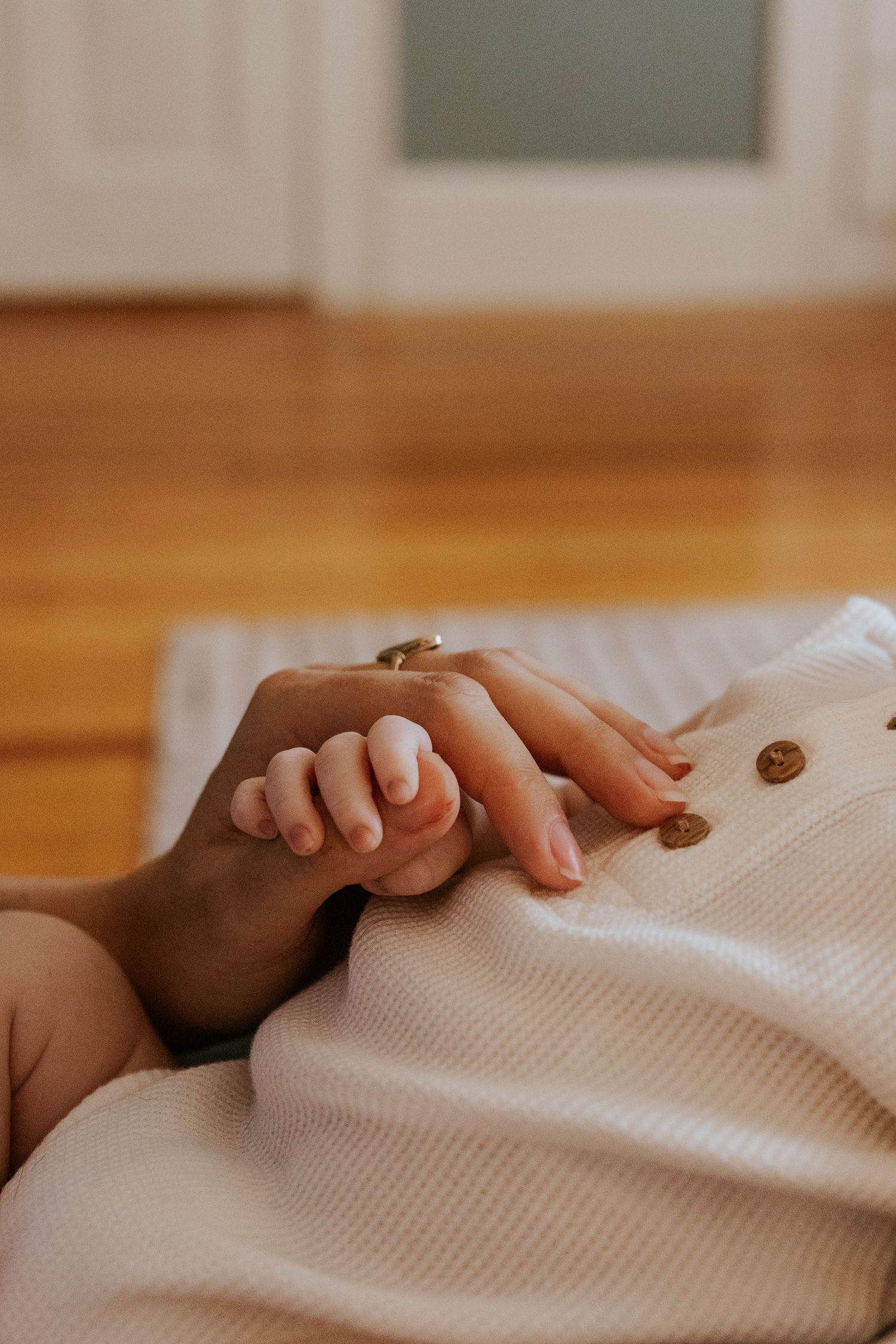 Close-up of newborn baby's tiny hand gently grasping mother's finger on white textured blanket.