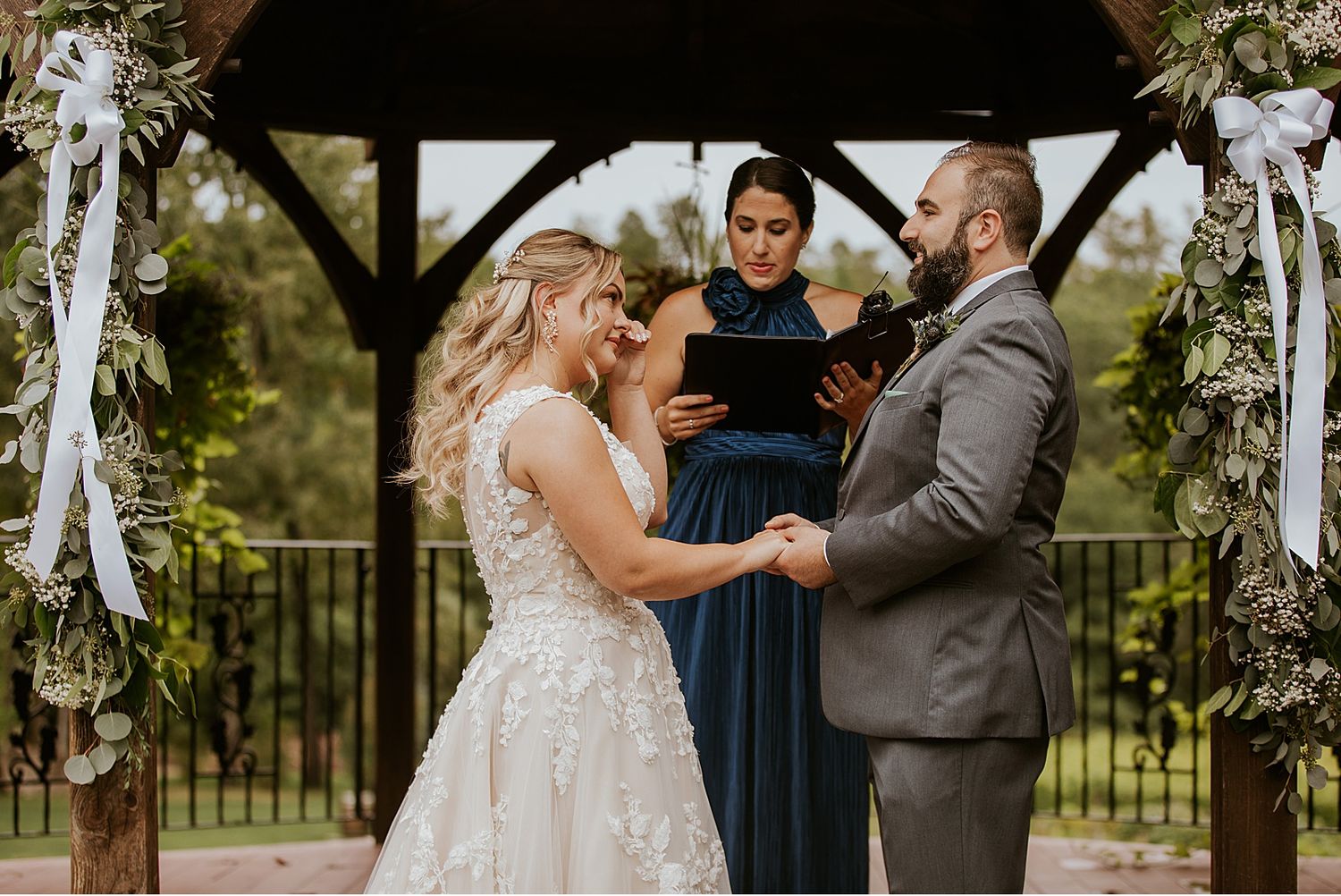 A romantic outdoor wedding ceremony with floral decorations and guests gathered in a natural setting.