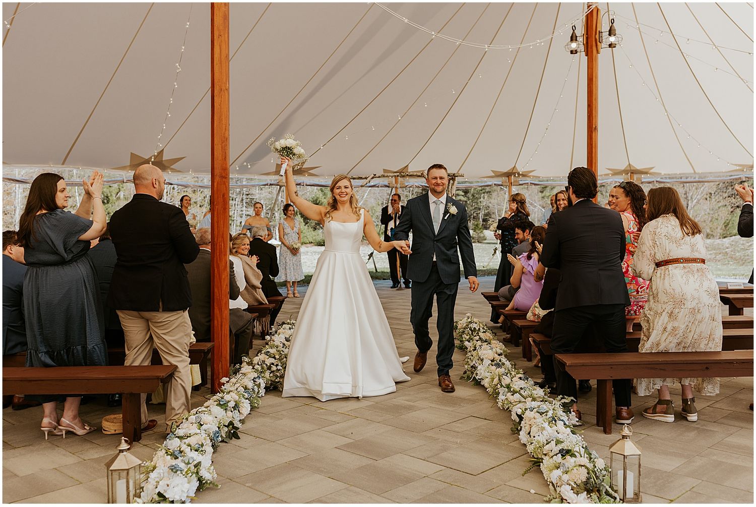 Wedding ceremony setup under a white tent with floral decorations lining the aisle.