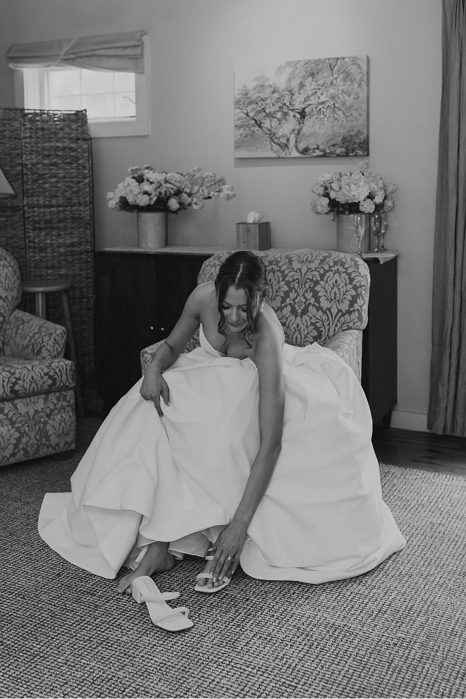 Wedding party members in white dresses relaxing on patterned chairs in a cozy room.