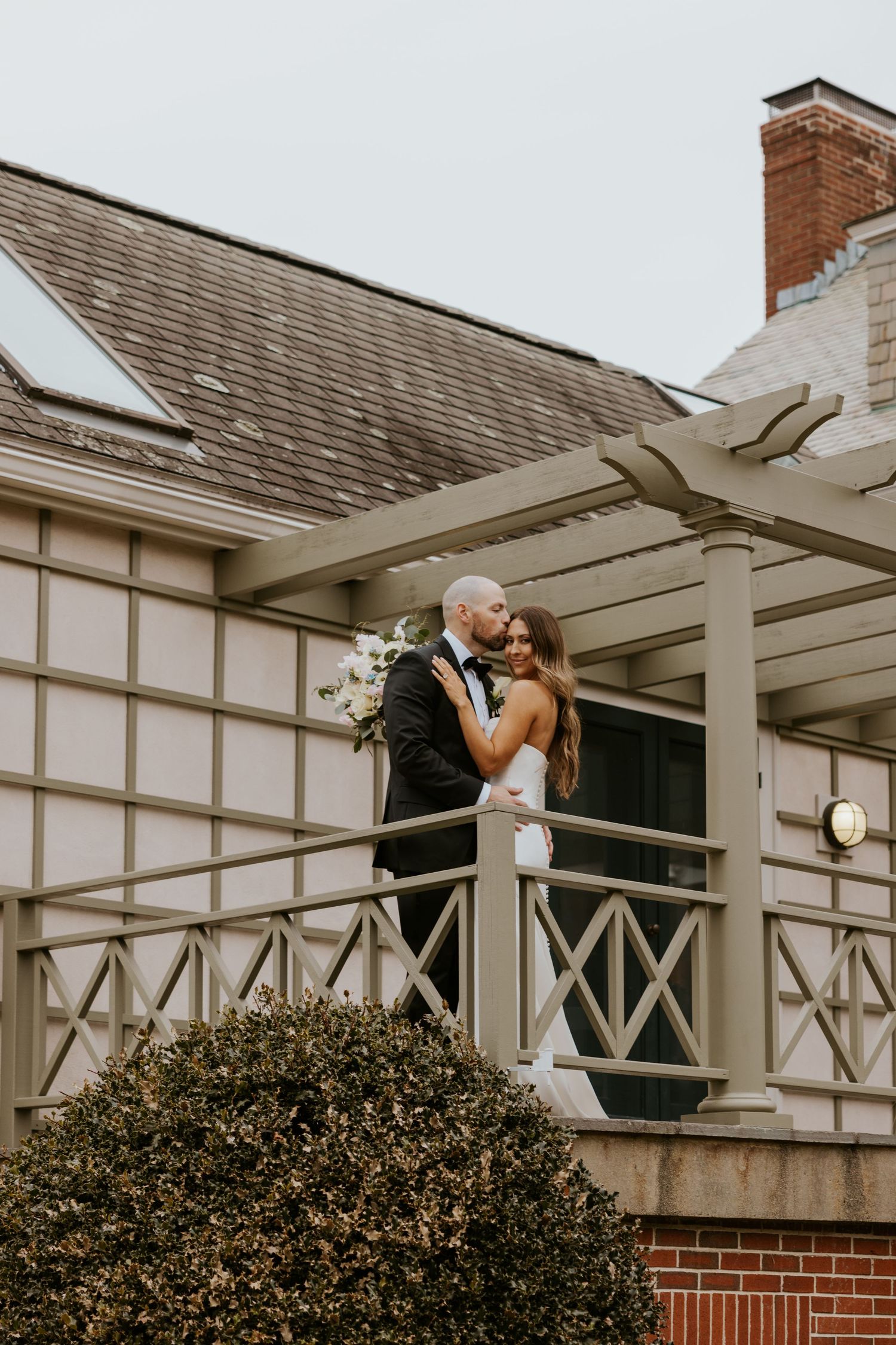 Couple sharing intimate moment on white pergola deck with brick and shingle architectural details.