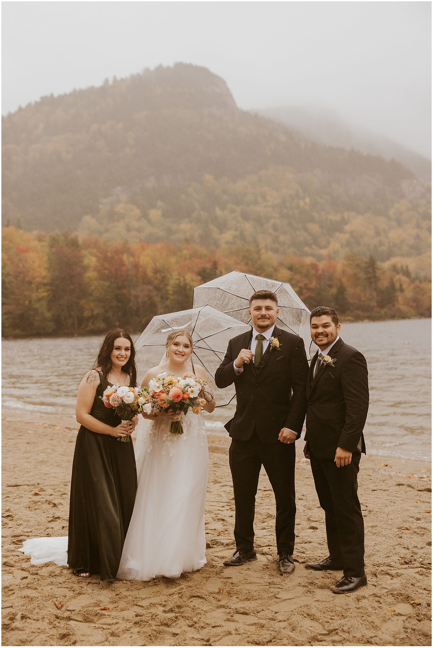 Wedding party poses with white umbrella on a beach with misty mountain backdrop during fall.