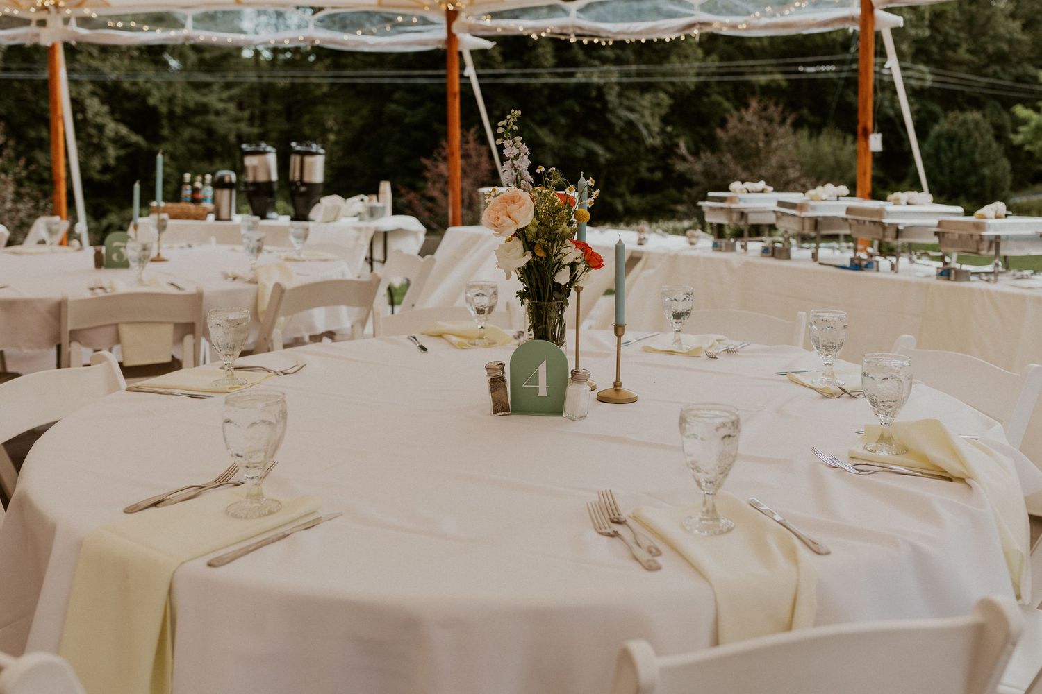 Elegant white tablescapes under wedding tent with floral centerpieces.