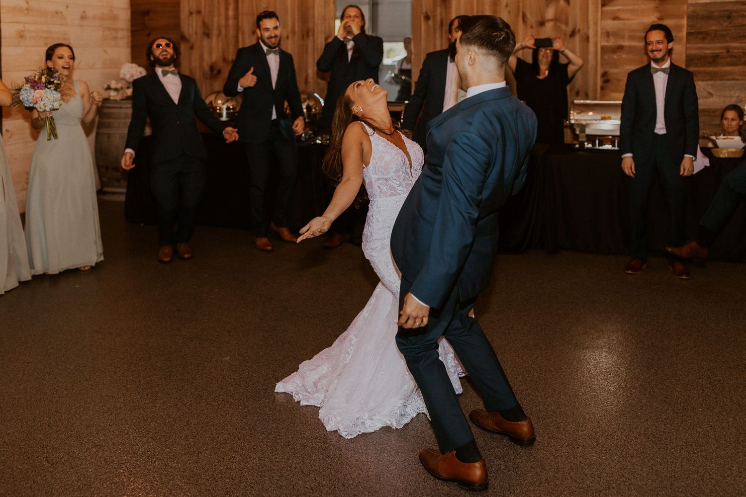 Couple performs their first dance in a rustic wooden venue with elegant lighting and wedding guests.