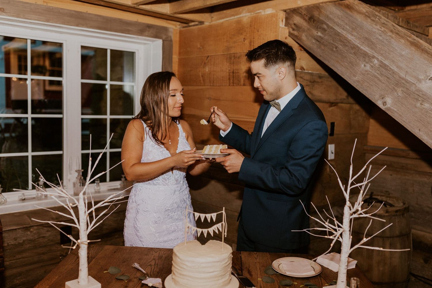 Couple enjoying a playful cake-cutting moment at their rustic barn wedding reception.