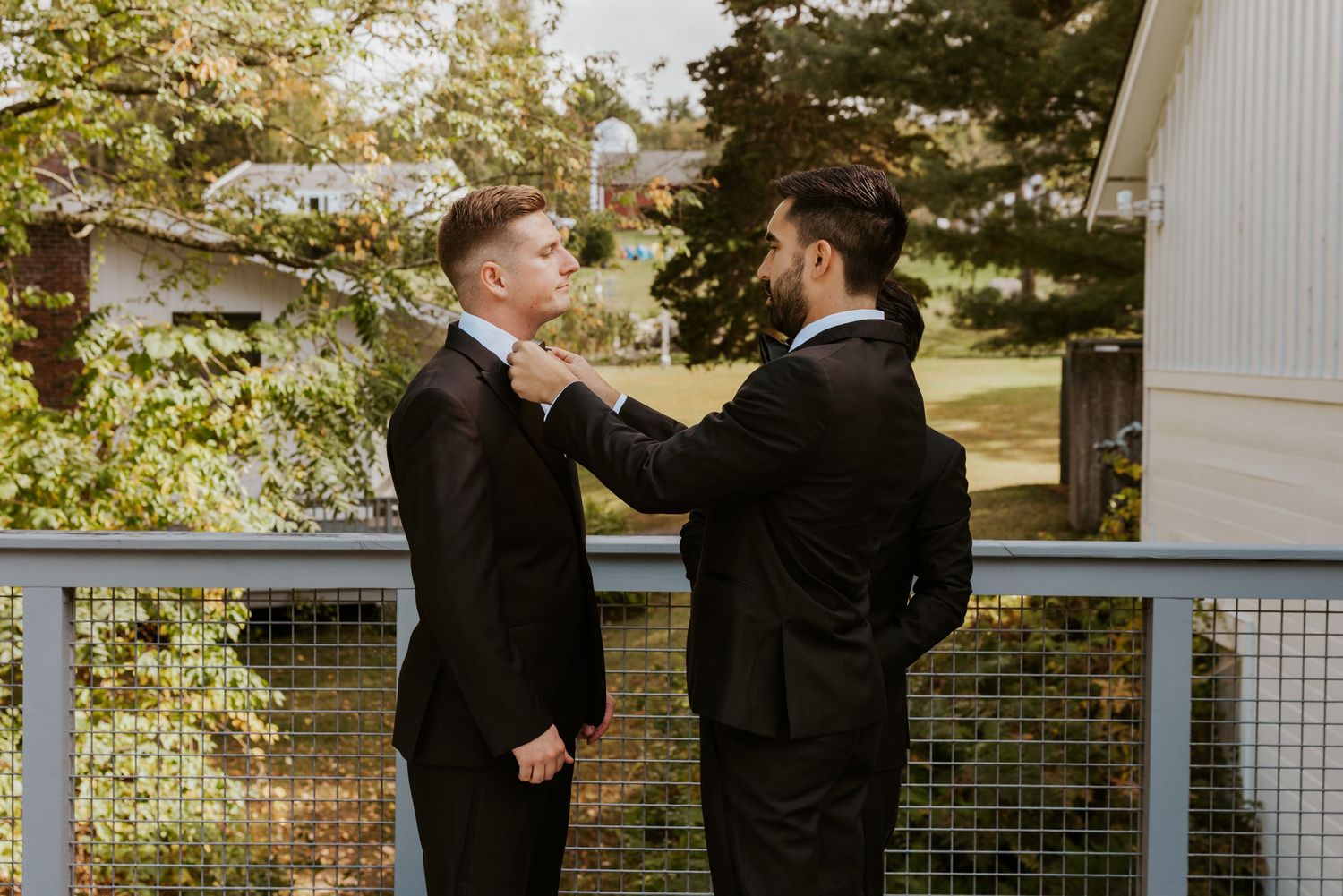 Groomsman adjusts another groomsmans tie on an outdoor deck before the wedding ceremony.