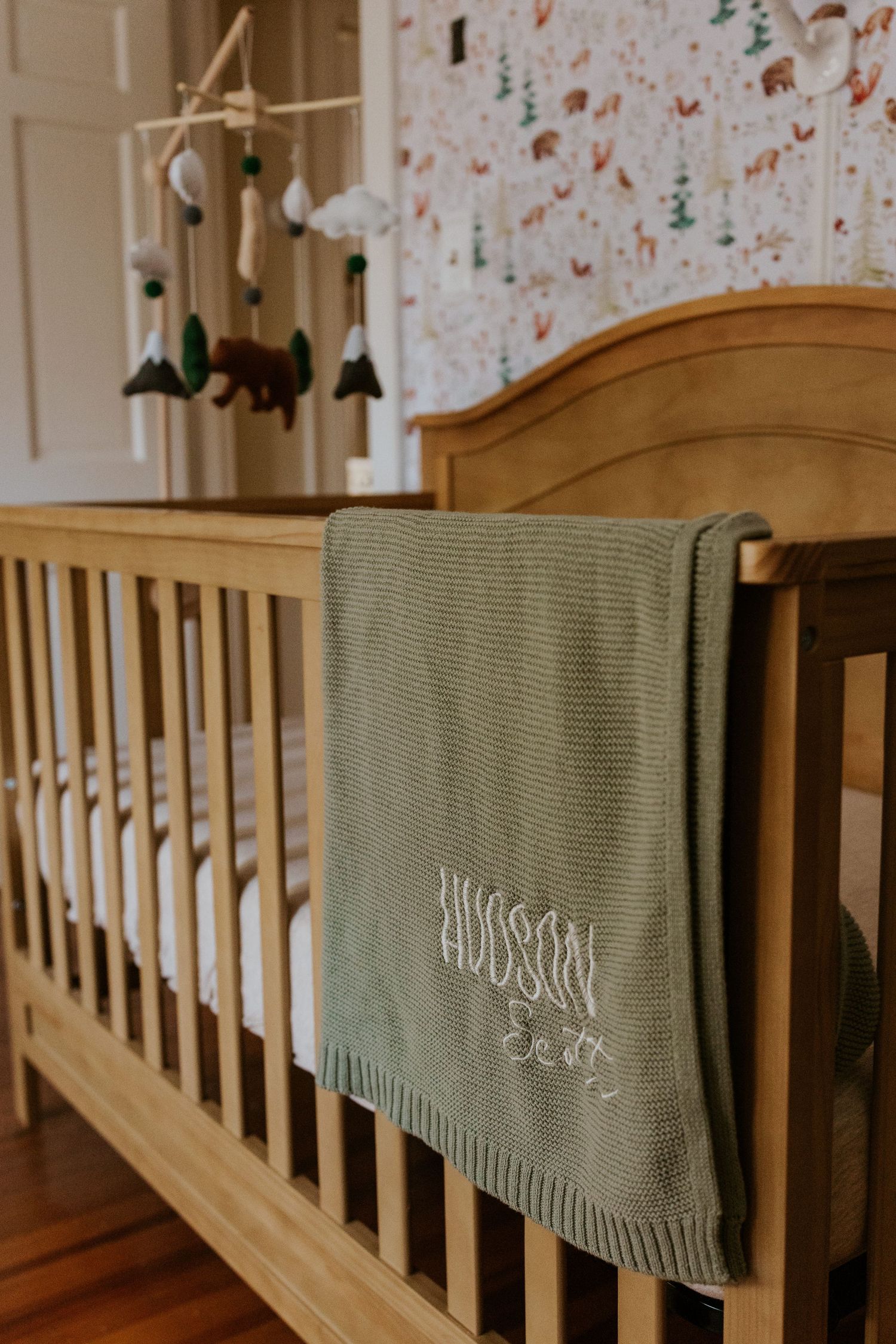 Wooden nursery crib with green knit personalized Hudson baby blanket and woodland animal mobile.