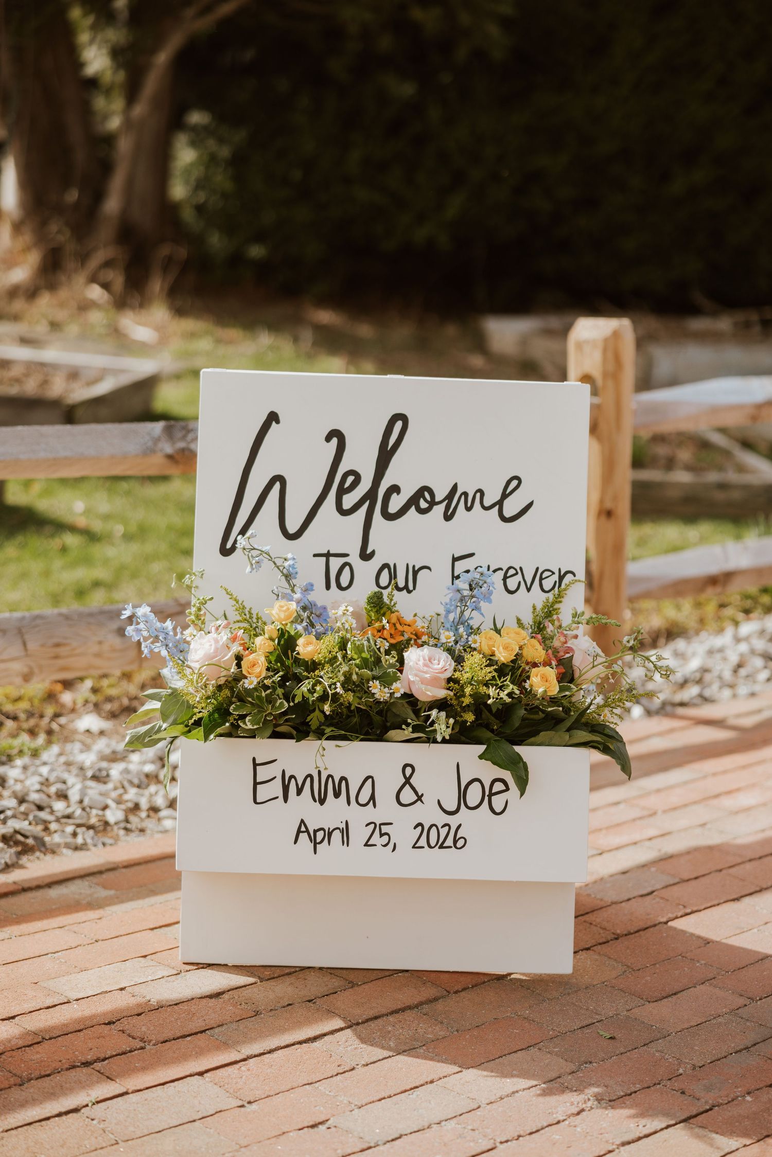 Wedding welcome sign reading Emma and Joe April 25 2026 decorated with colorful fresh flowers.