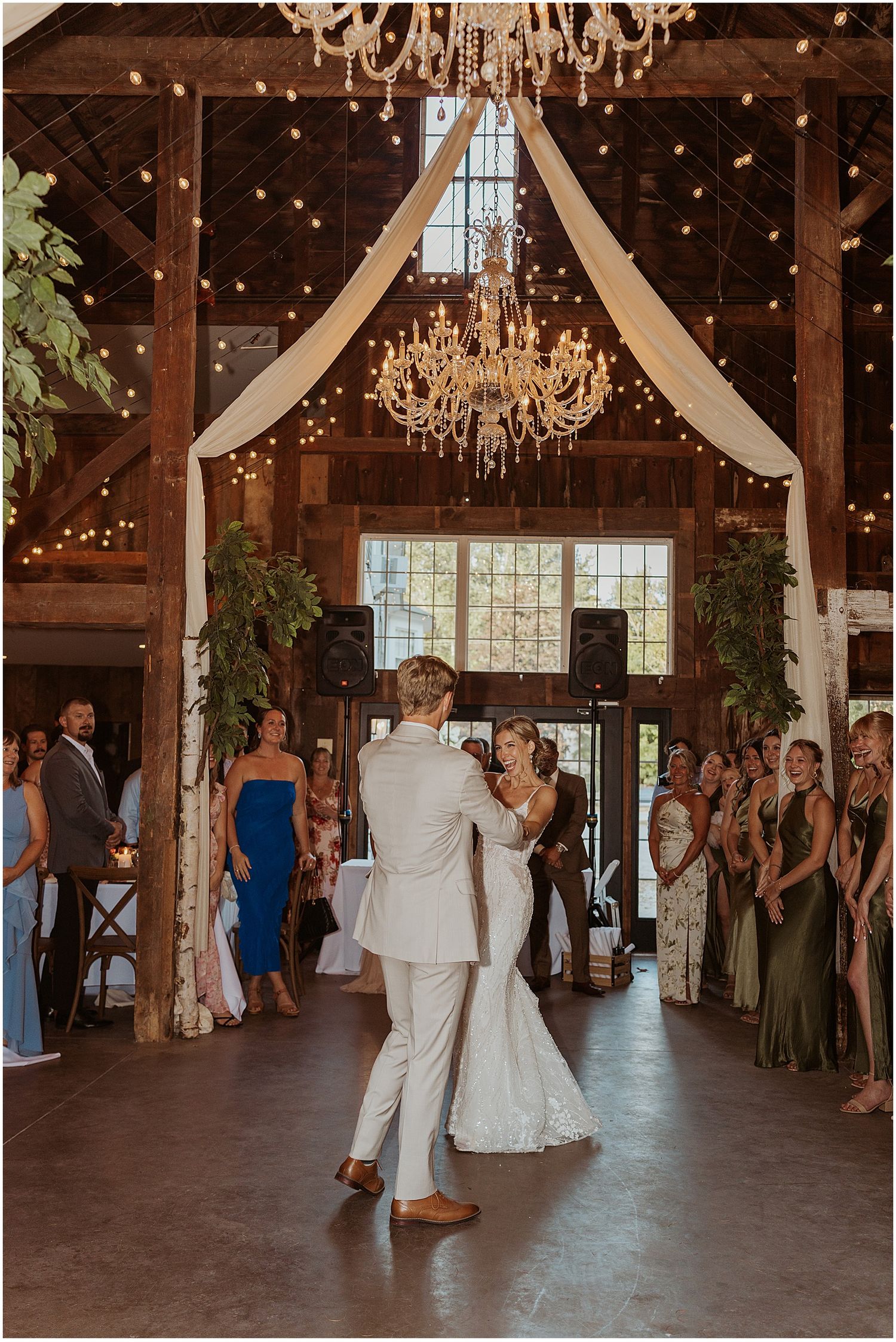 Couple sharing their first dance in a rustic barn venue with twinkling lights and chandeliers.