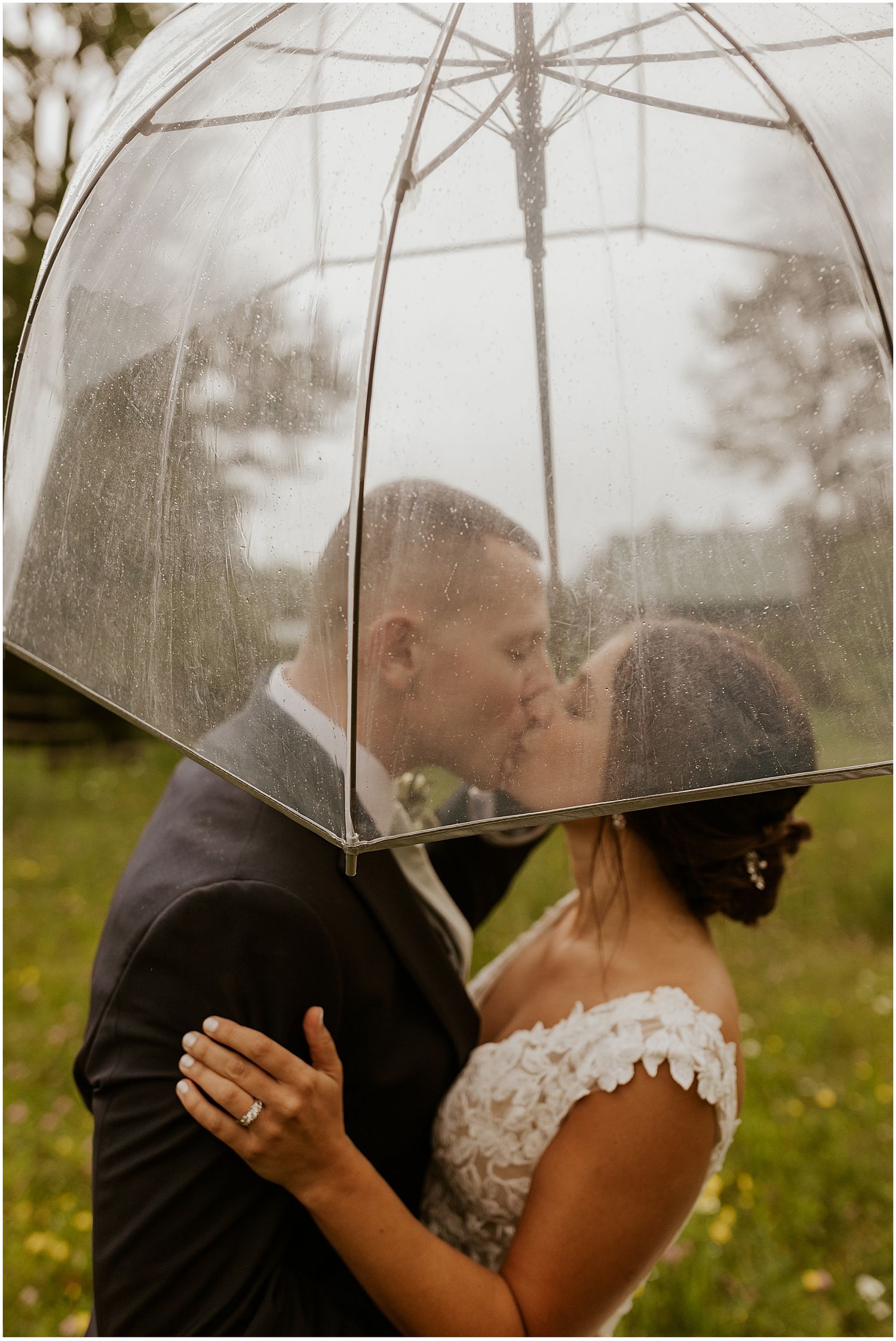 A tender moment shared under a clear umbrella in a meadow setting.