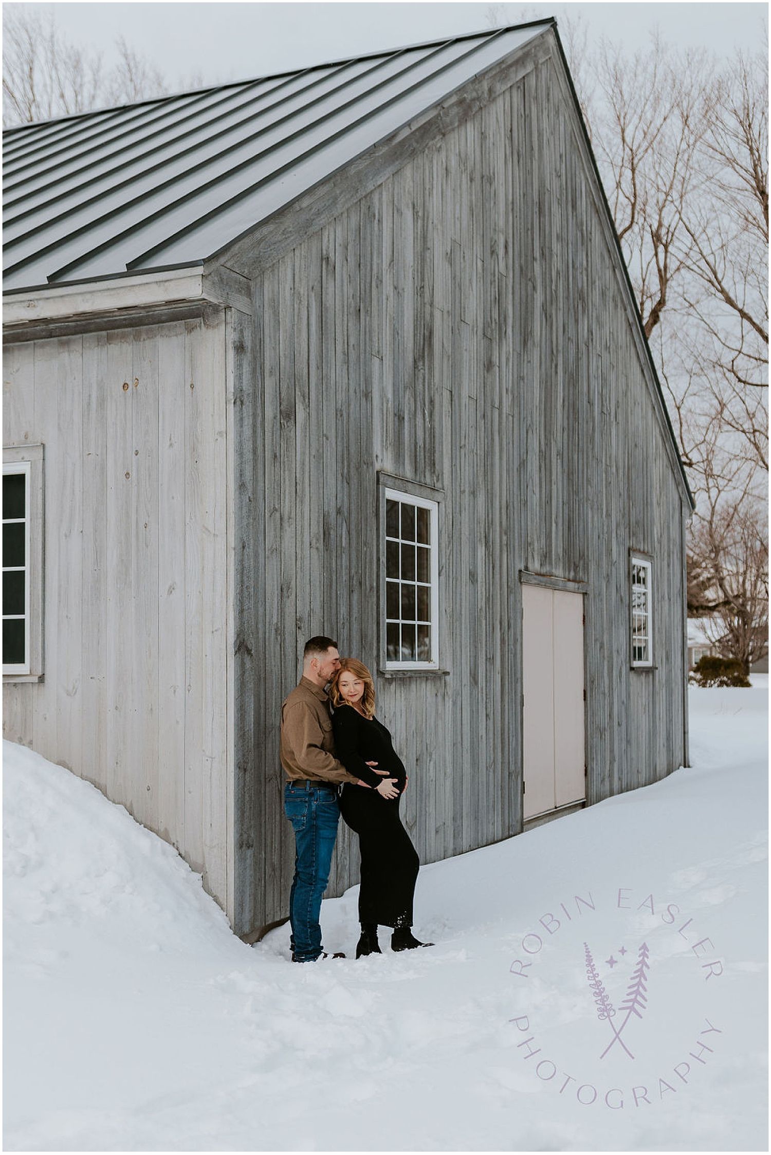 Snow-covered rustic wooden barn with white siding and windows in winter.
