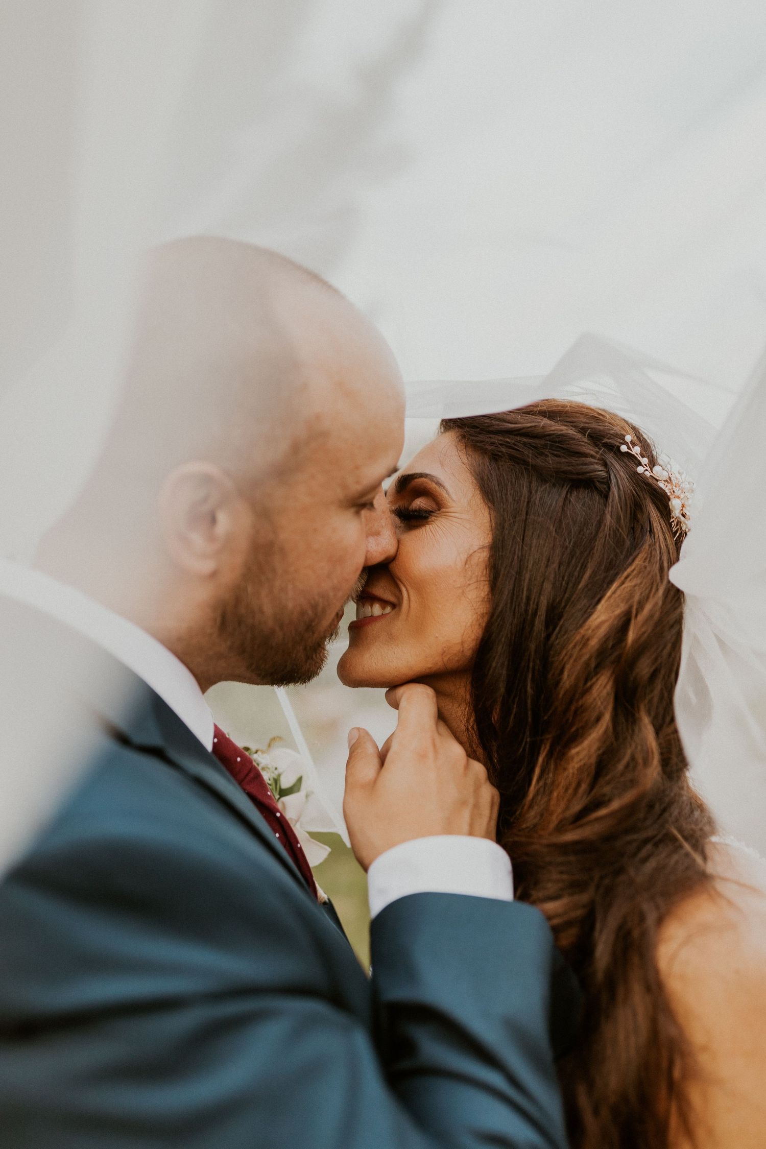 Intimate wedding kiss captured in soft, dreamy lighting against a bright background.
