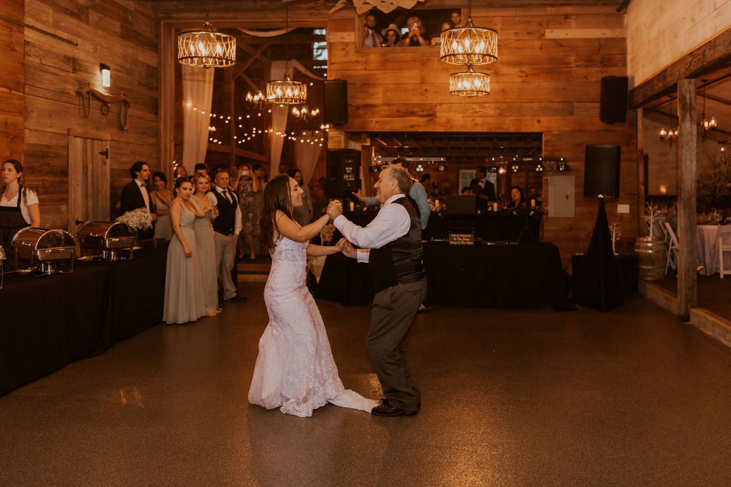 Wedding dance floor moments in a rustic barn venue with chandeliers and wooden walls.