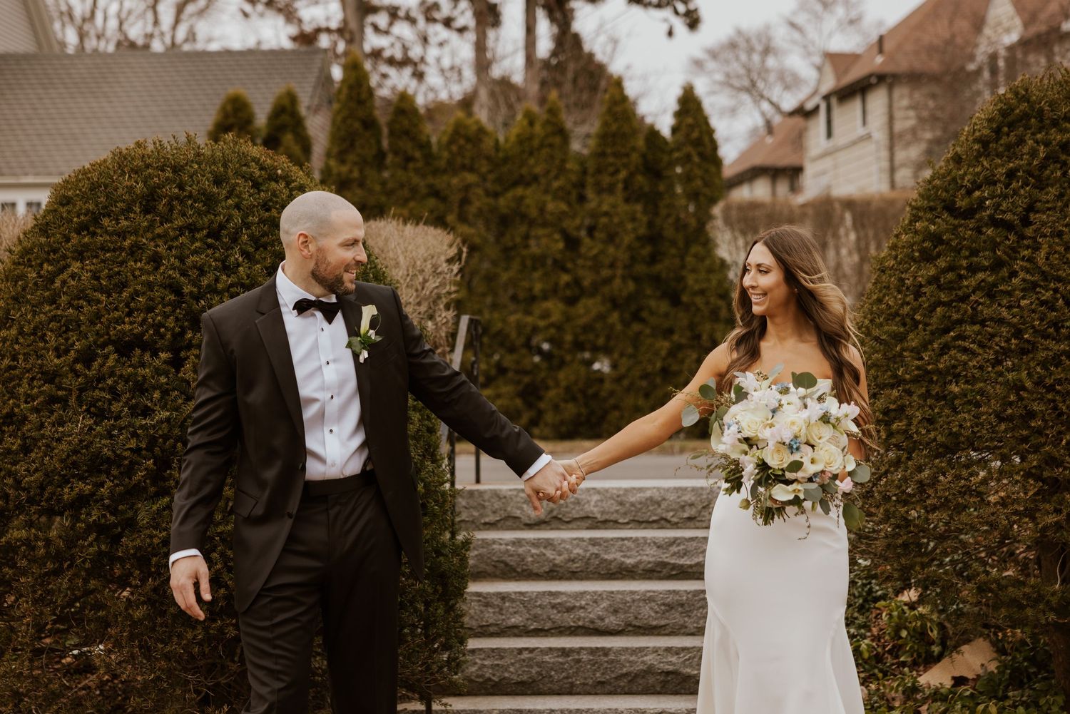 Romantic wedding couple embracing in front of manicured garden hedges at outdoor venue.