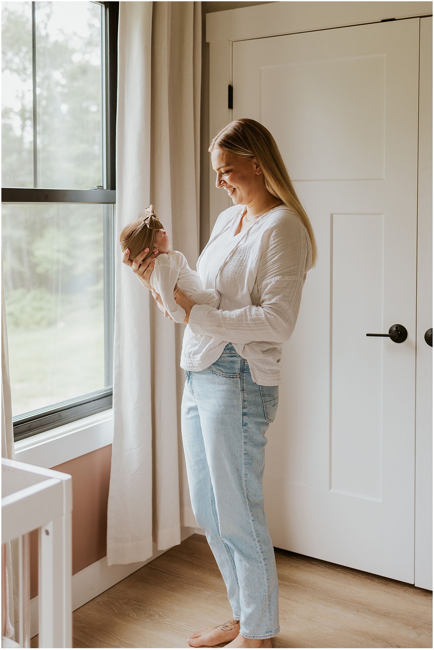 NH mom wearing a light sweater and jeans taking portrait photos at home with her newborn