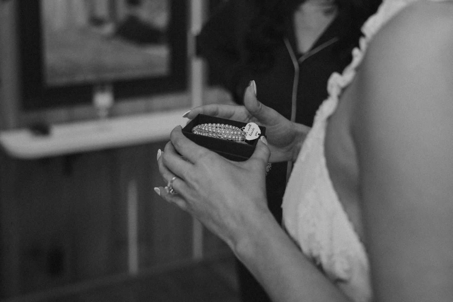 Bride holding an open jewelry box with a diamond ring in a black and white wedding photo.