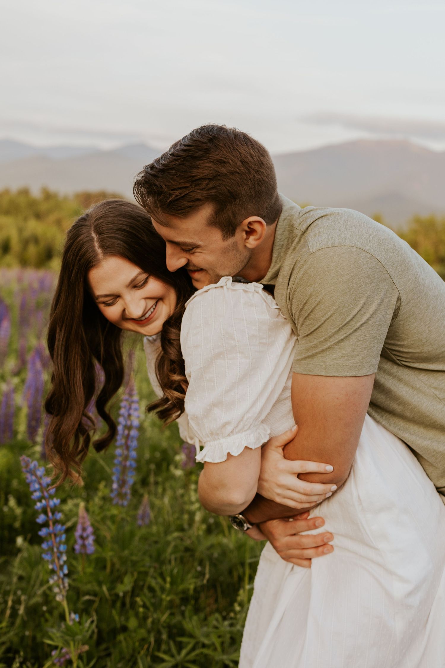 Man joyfully hugging woman from behind as she laughs in a colorful wildflower field.