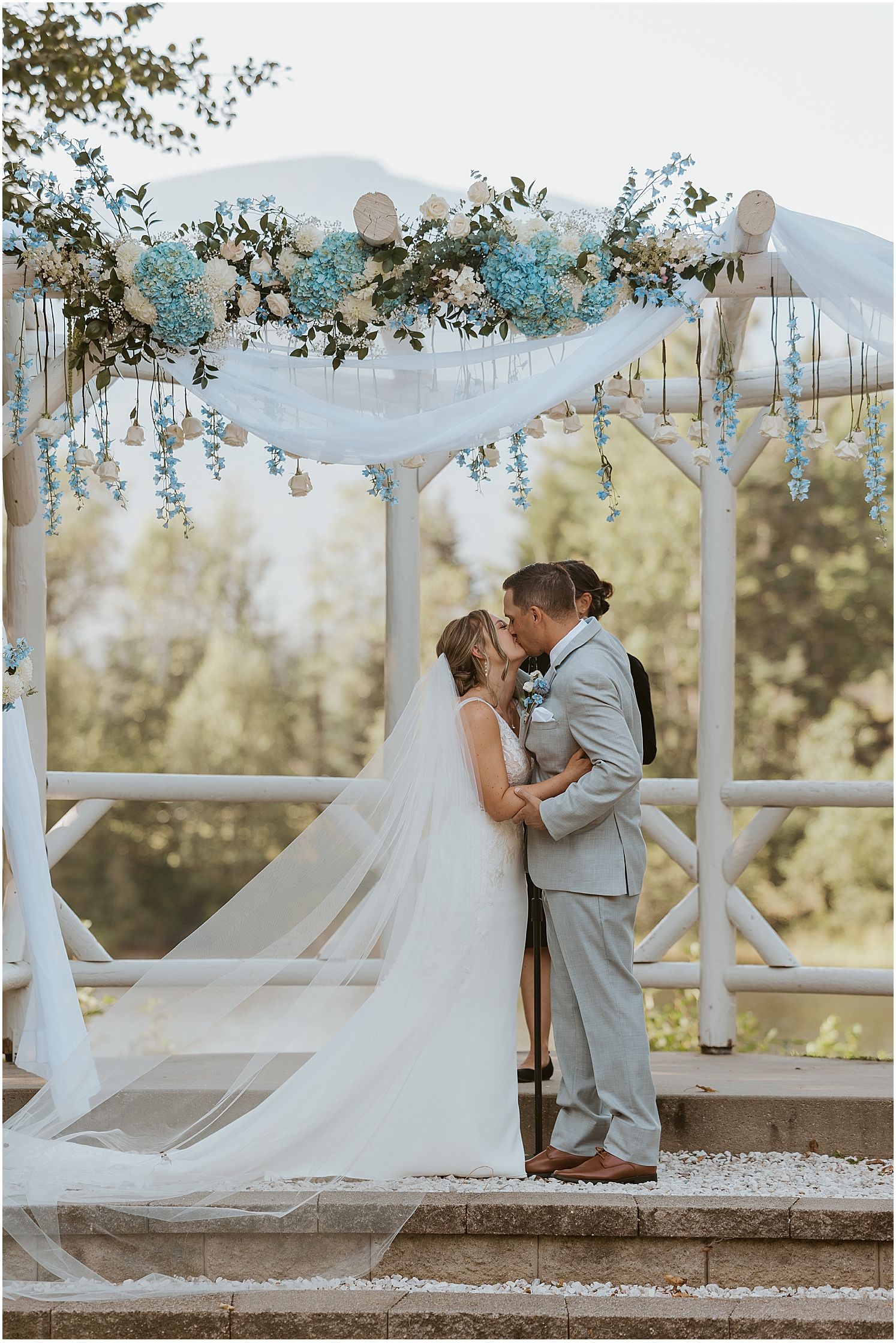 Romantic wedding ceremony moment under a decorated white gazebo at sunset.