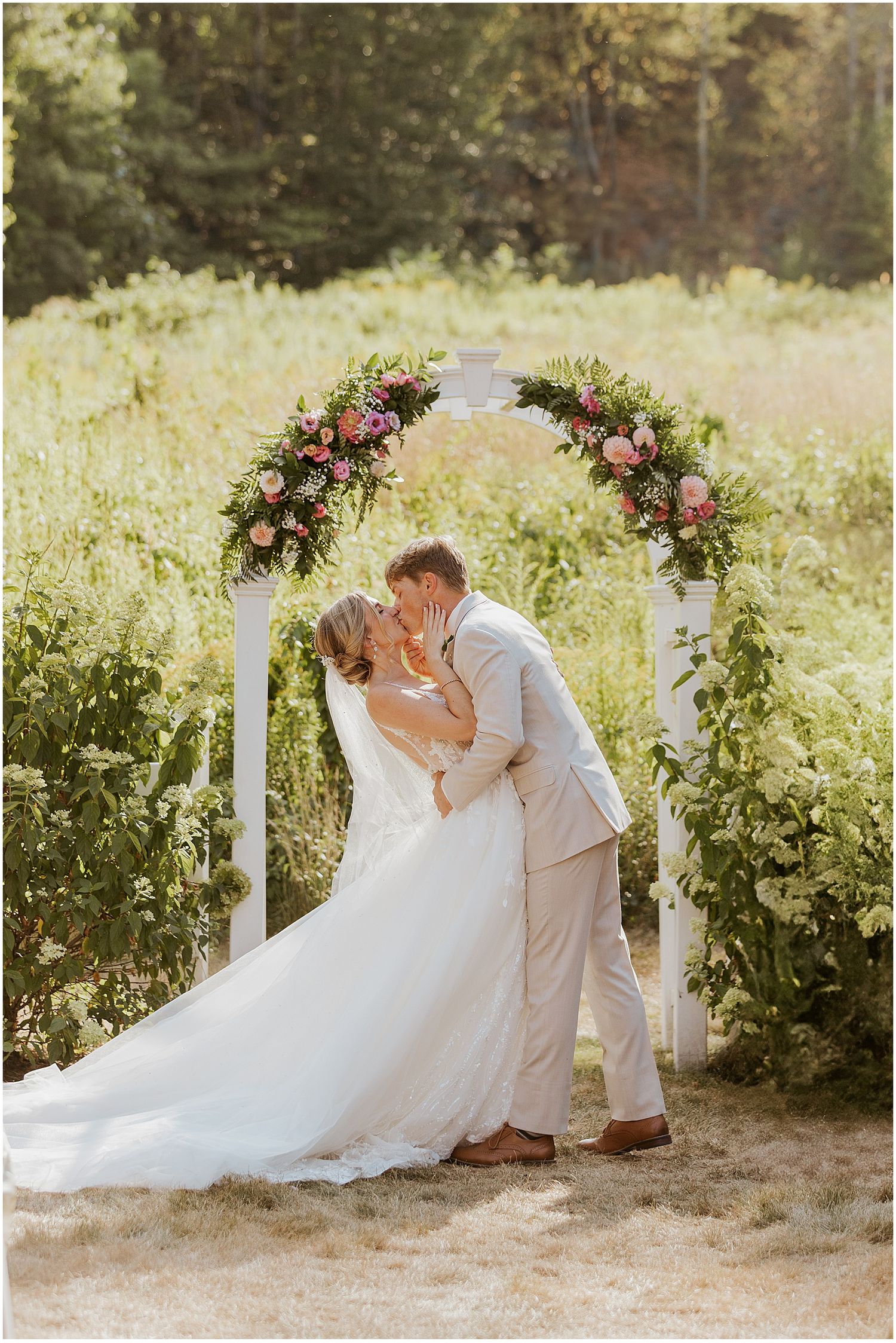 Wedding couple shares a romantic moment under floral arches in a sunlit garden.