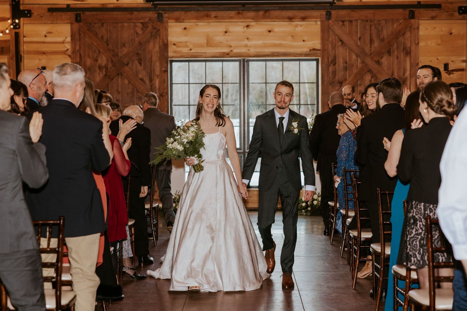 Wedding ceremony guests seated in wooden chairs inside a rustic barn venue.