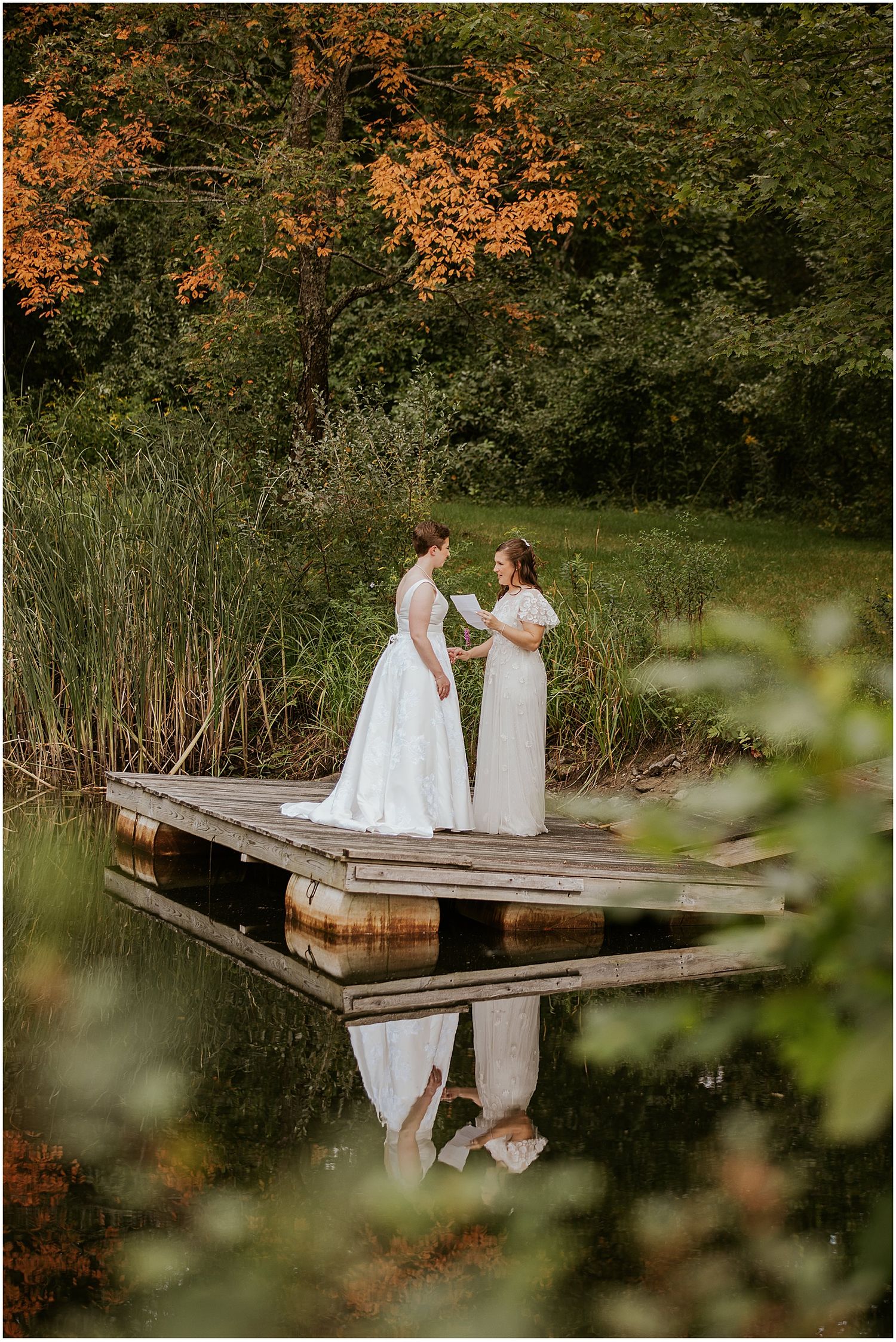 Brides sharing a first look on a wooden dock at Longlook Farm in New Hampshire