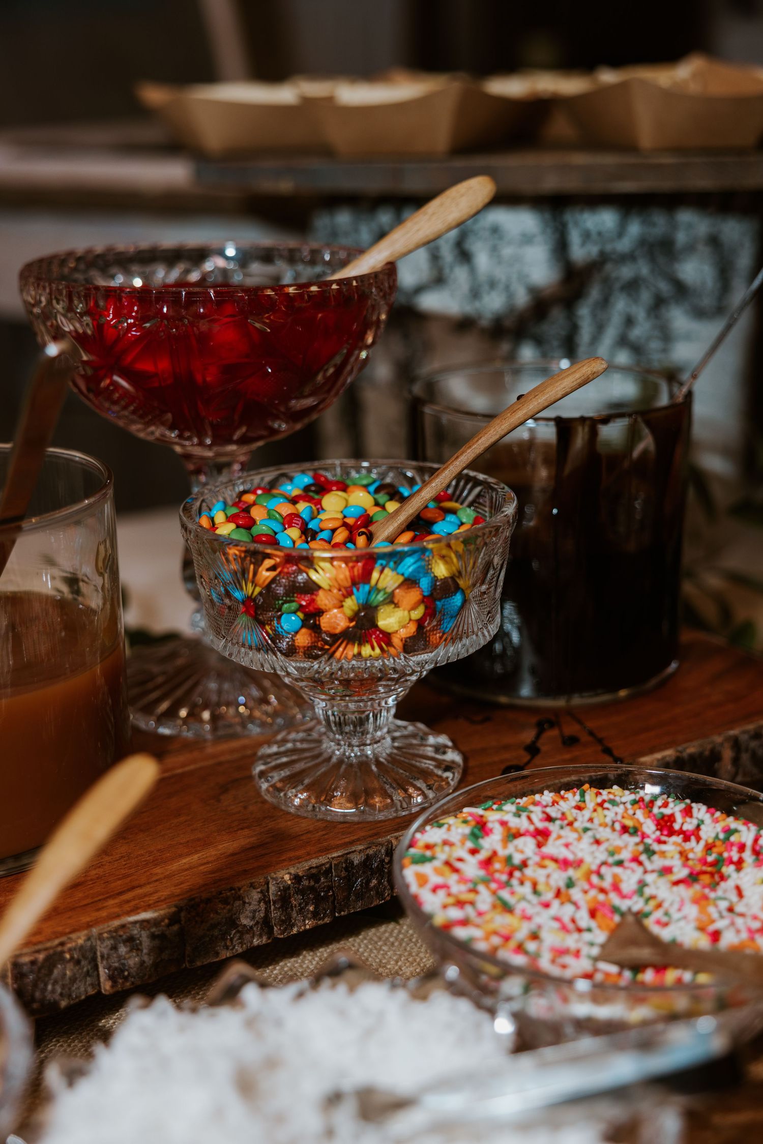 Colorful candy and dessert display with glass bowls on wooden table at wedding reception.