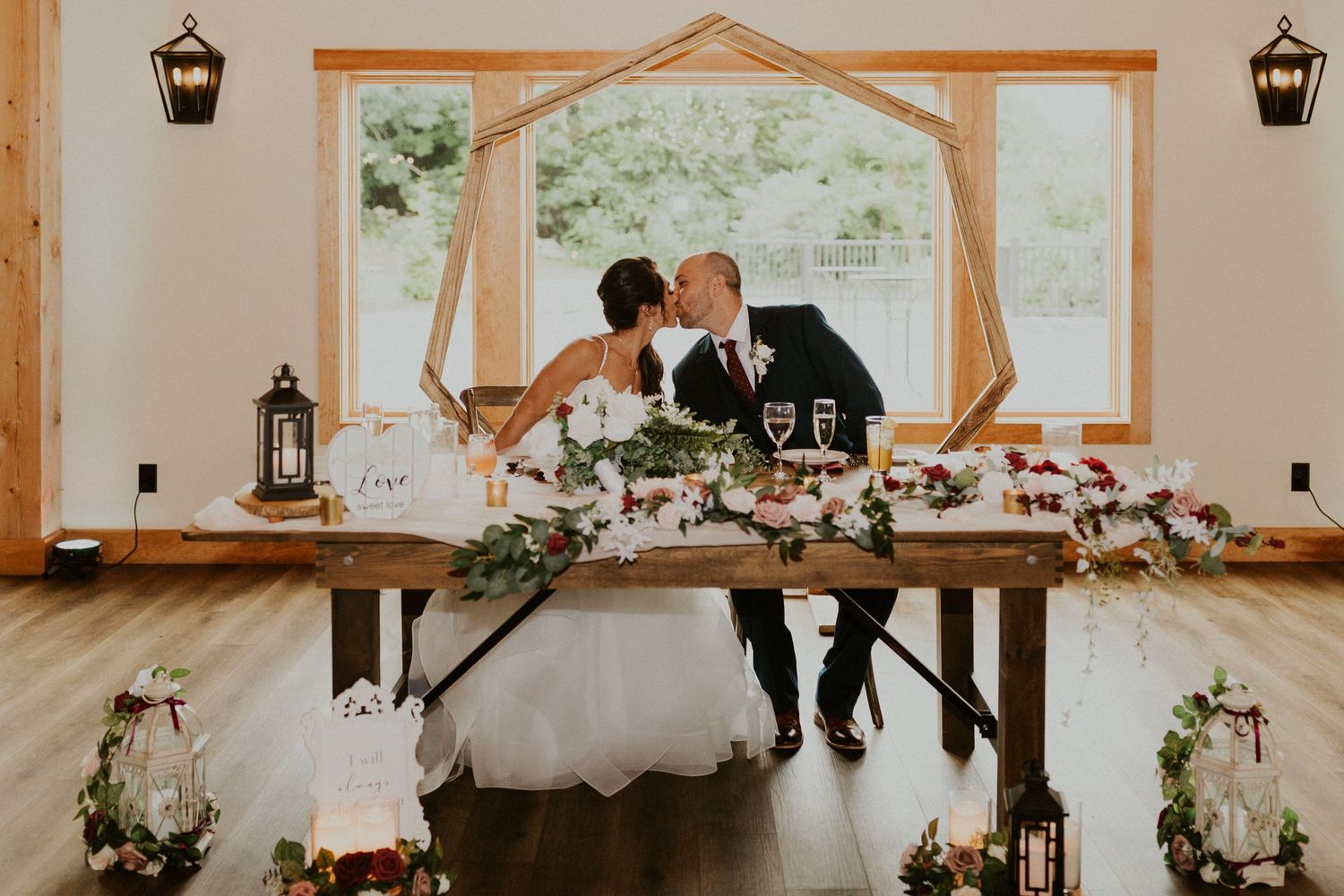 Rustic wedding venue decorated with lanterns and floral arrangements along wooden beams.