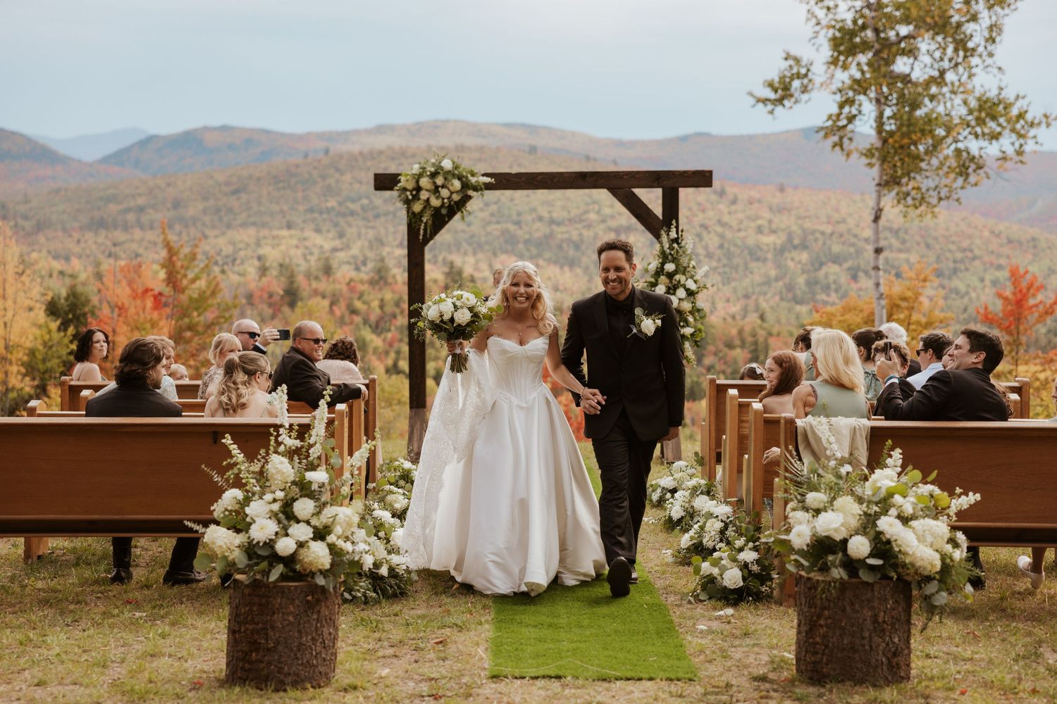 Bride and groom walk down the aisle at an outdoor fall wedding ceremony with mountain views.