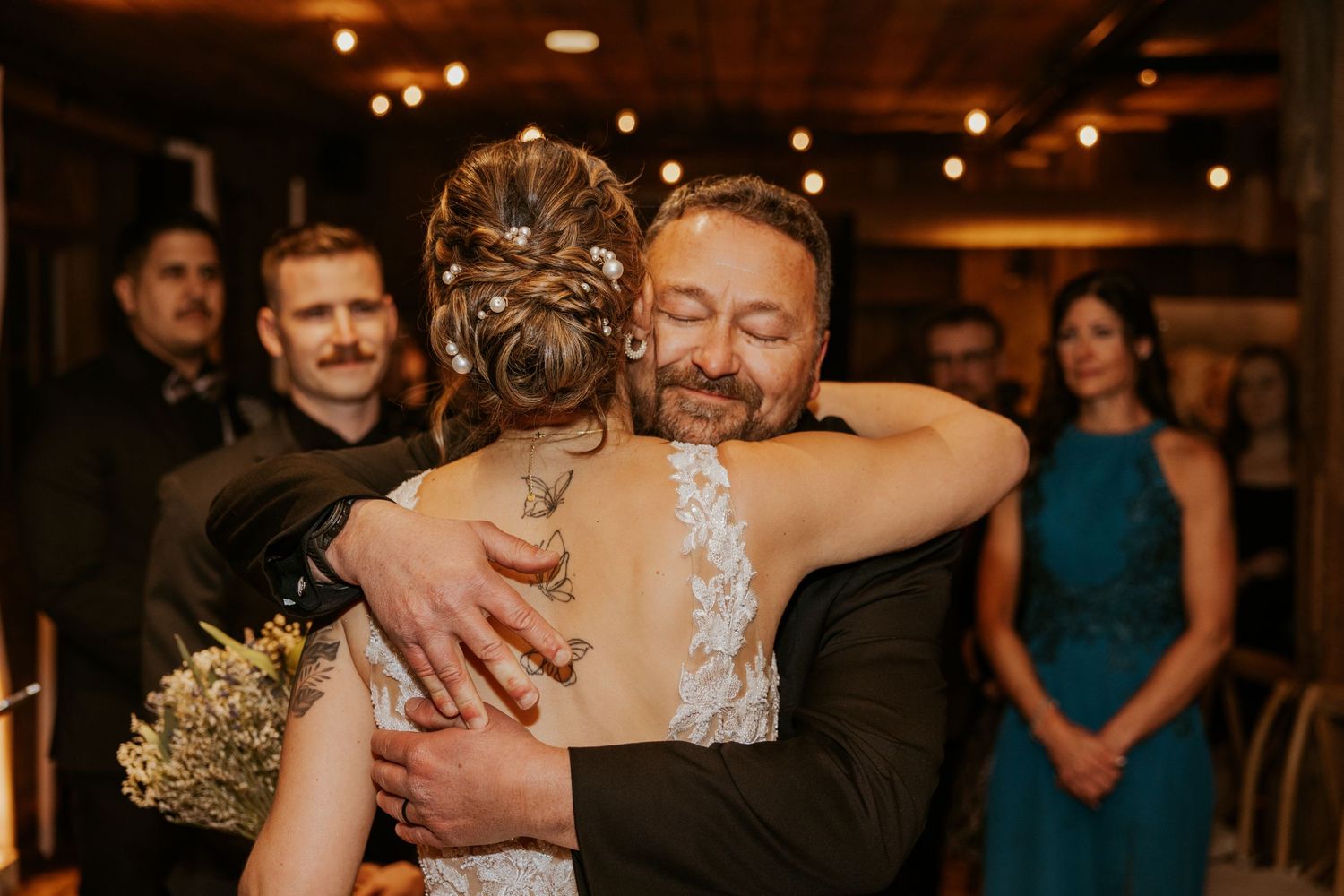 Bride and groom share an emotional hug during wedding reception in rustic venue.