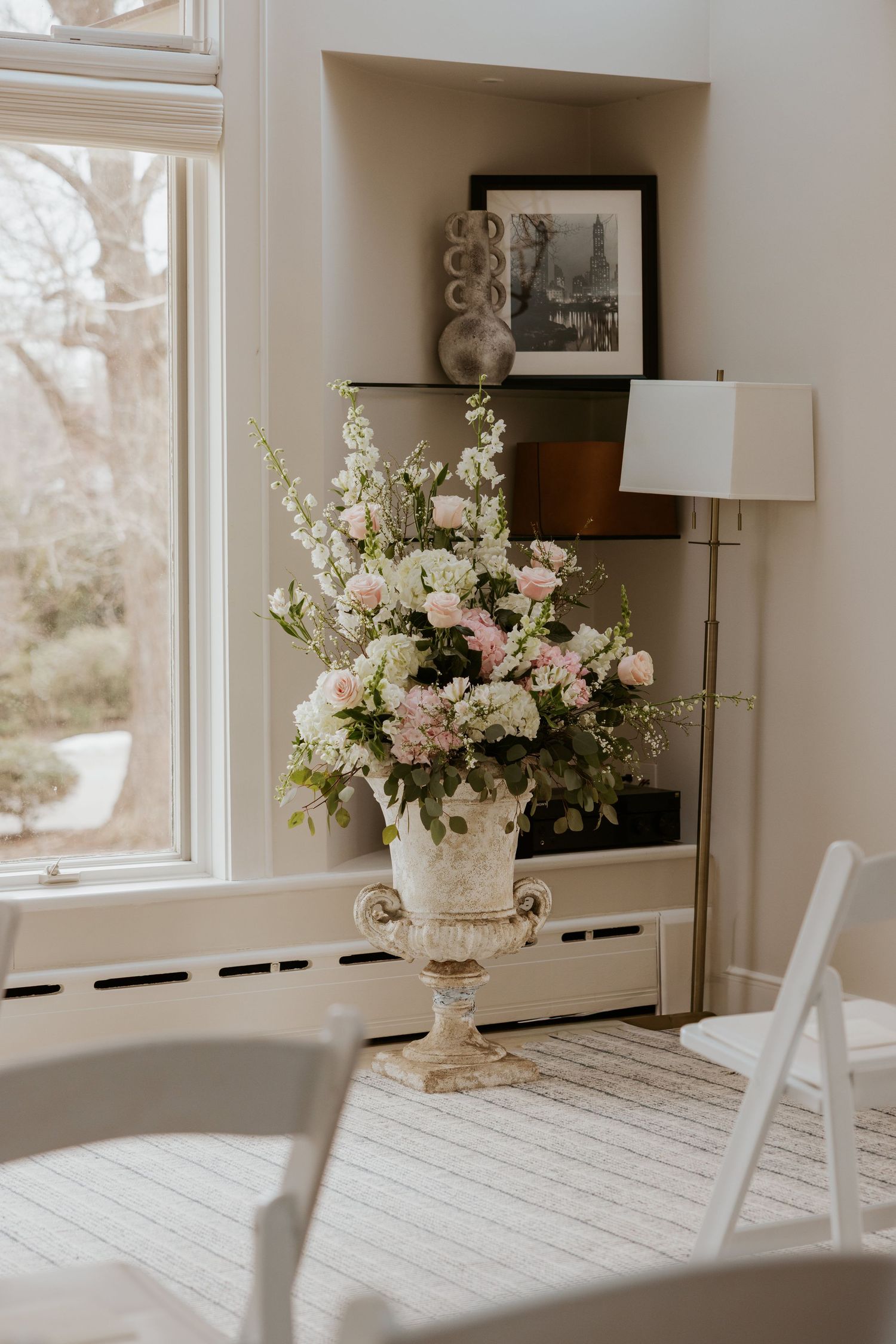 White dining table with floral centerpieces near windows in a bright, modern interior setting.