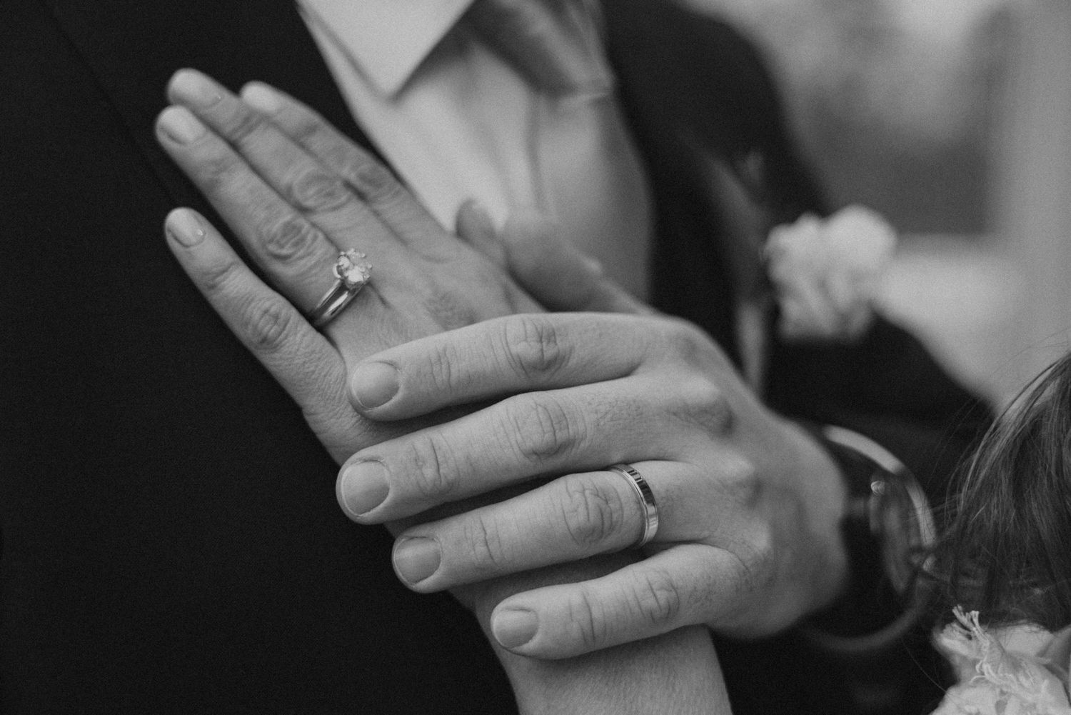 Black and white close-up of hands with wedding rings during an intimate ceremony moment.