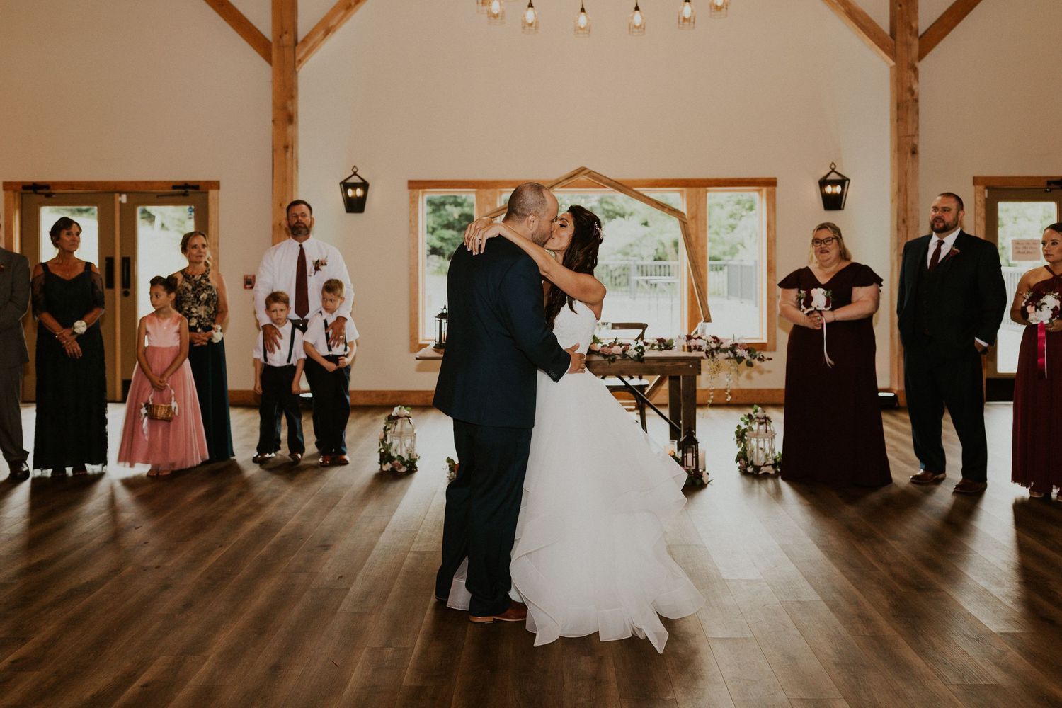 Spacious barn wedding venue with wooden beams and hardwood floors during a reception.