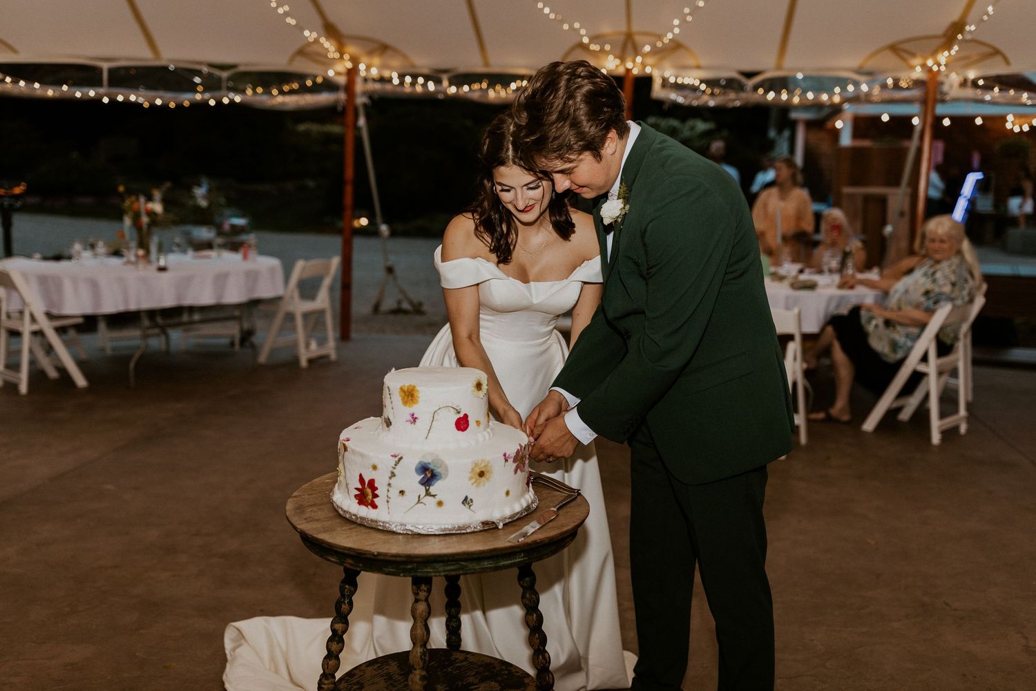 Wedding reception scene with string lights and cake cutting ceremony.