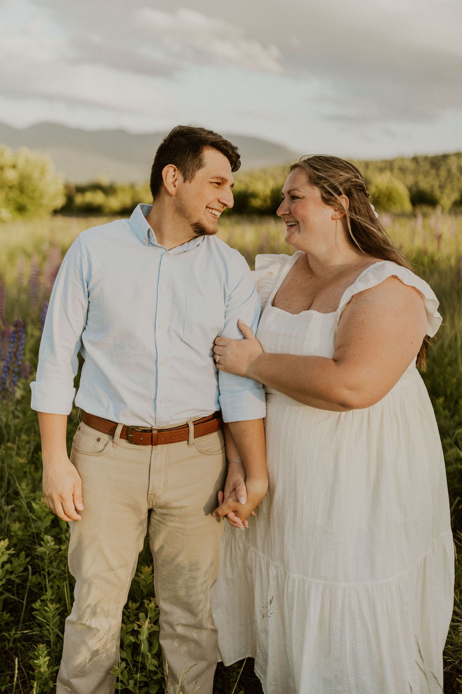 Terise hugging onto Jose's arm and smiling during an engagement photoshoot in the lupine fields of Sugar Hill NH.