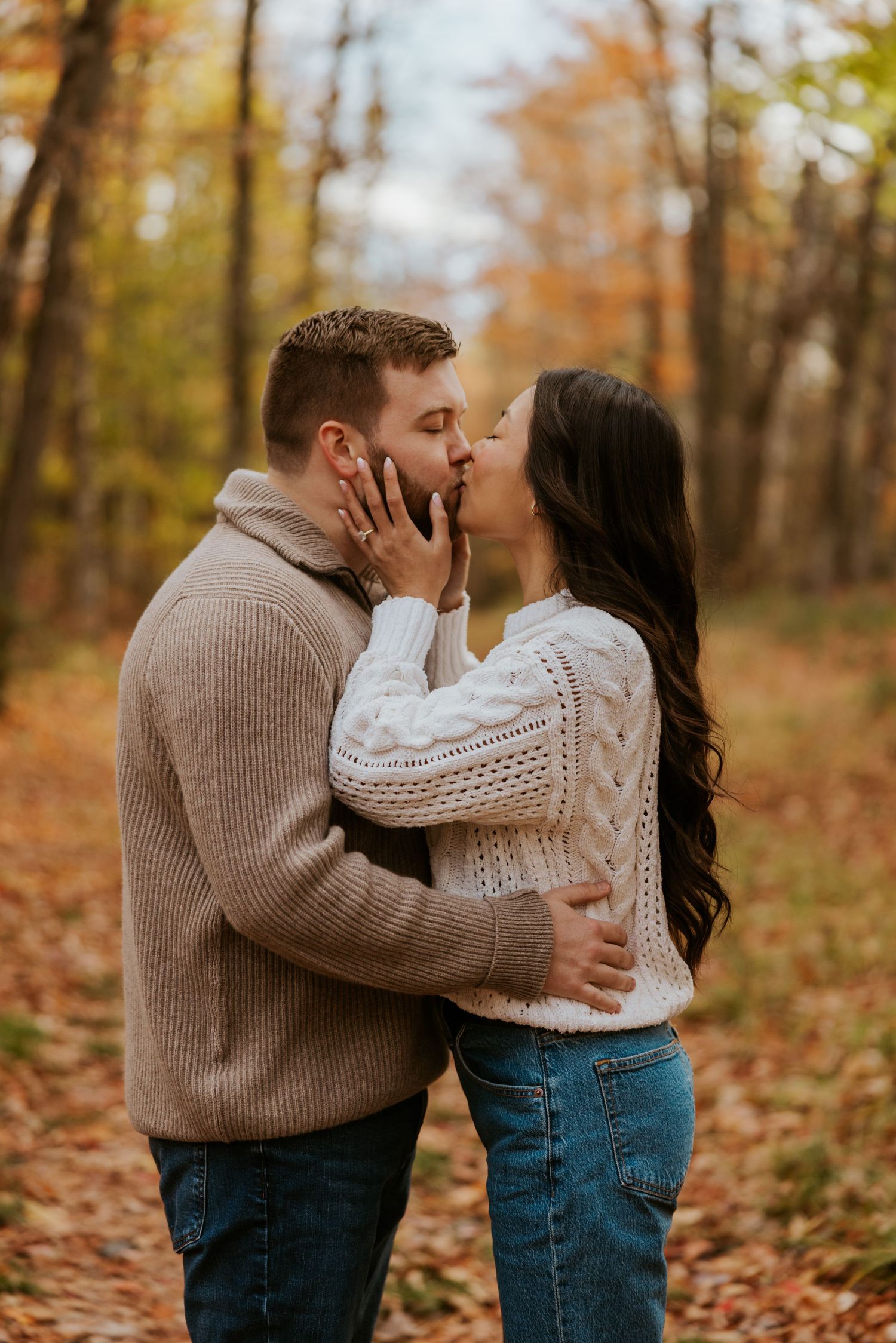 Couple sharing a romantic kiss surrounded by fall foliage in the woods.