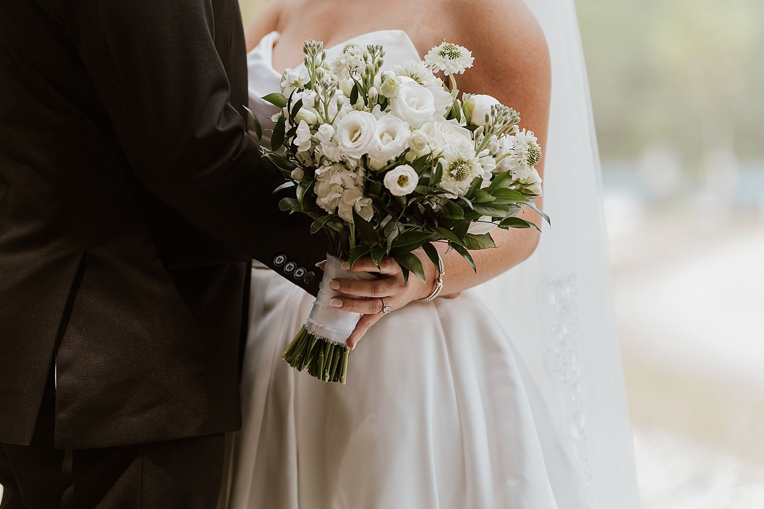 Bride and groom holding a white rose and greenery wedding bouquet in an elegant close-up shot.