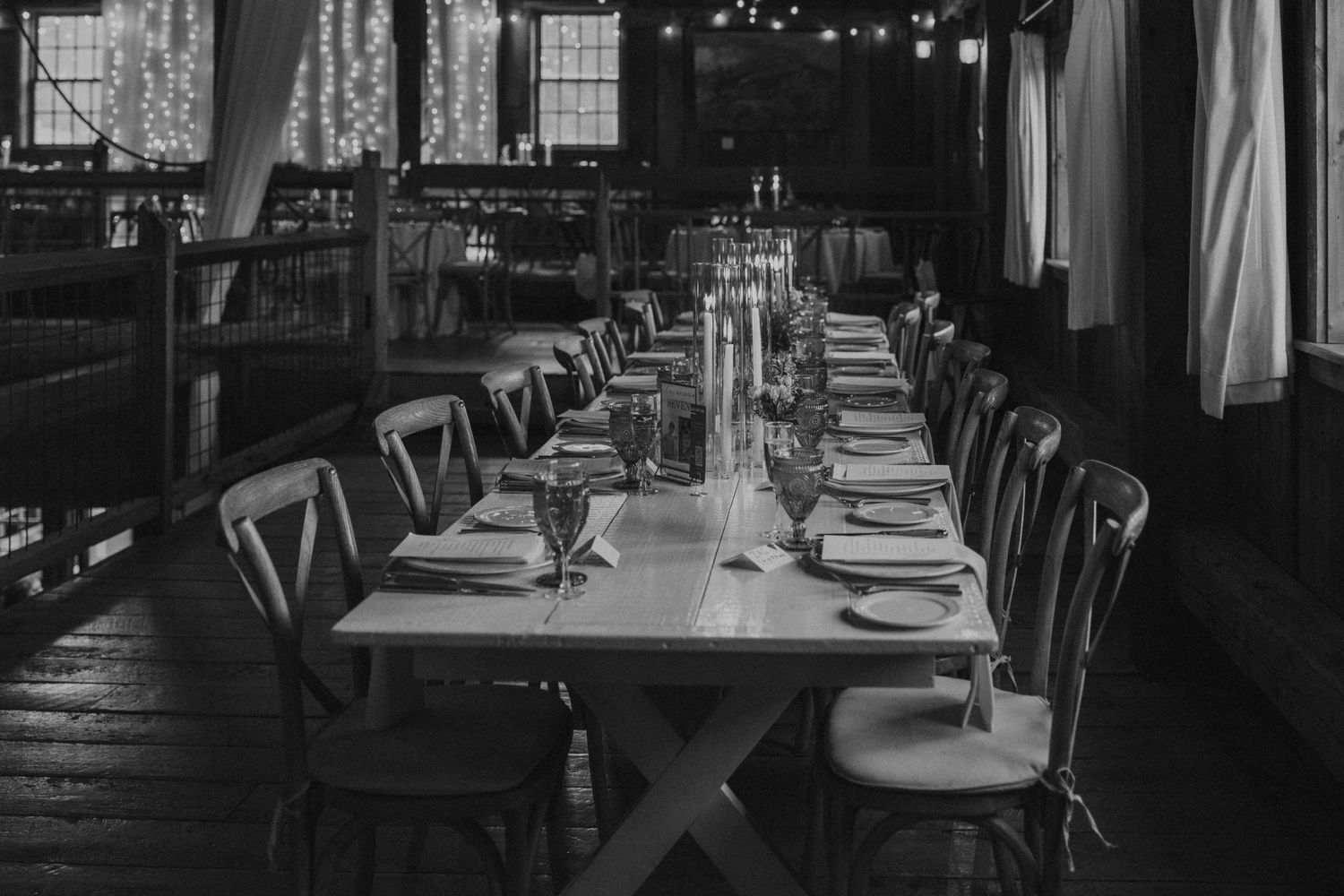 Elegant long reception table set with candles and dinnerware in a rustic venue, captured in black and white.