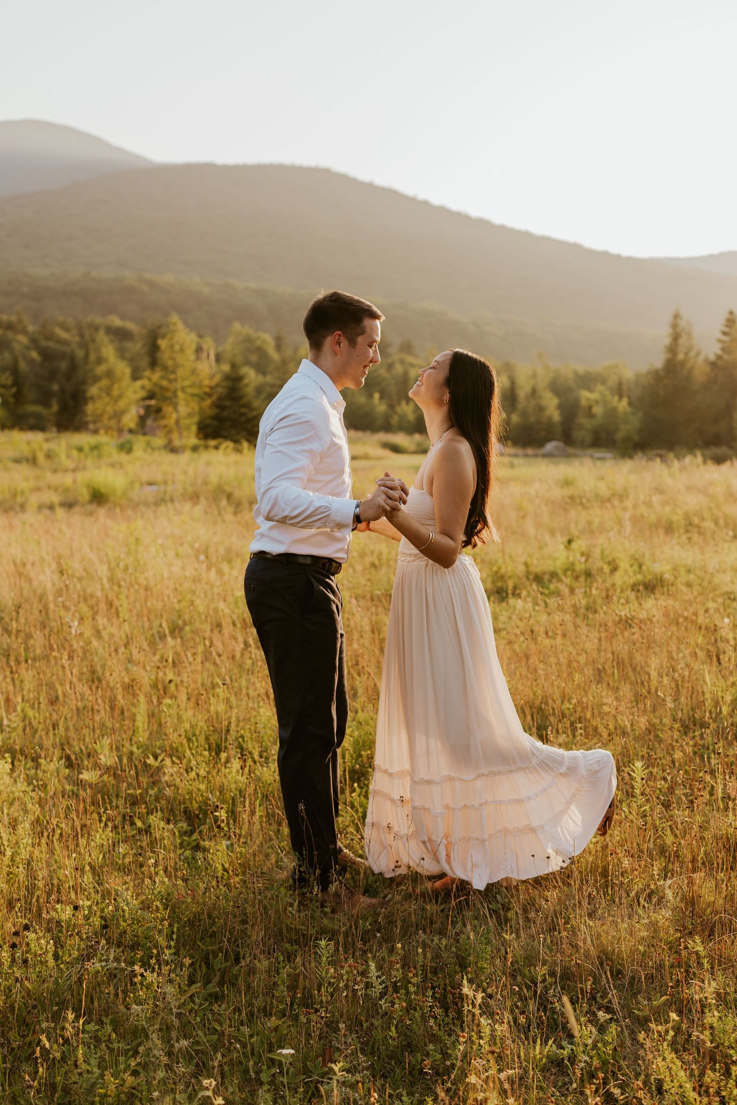 Couple dances together holding hands in glowing sunset field with mountain views.