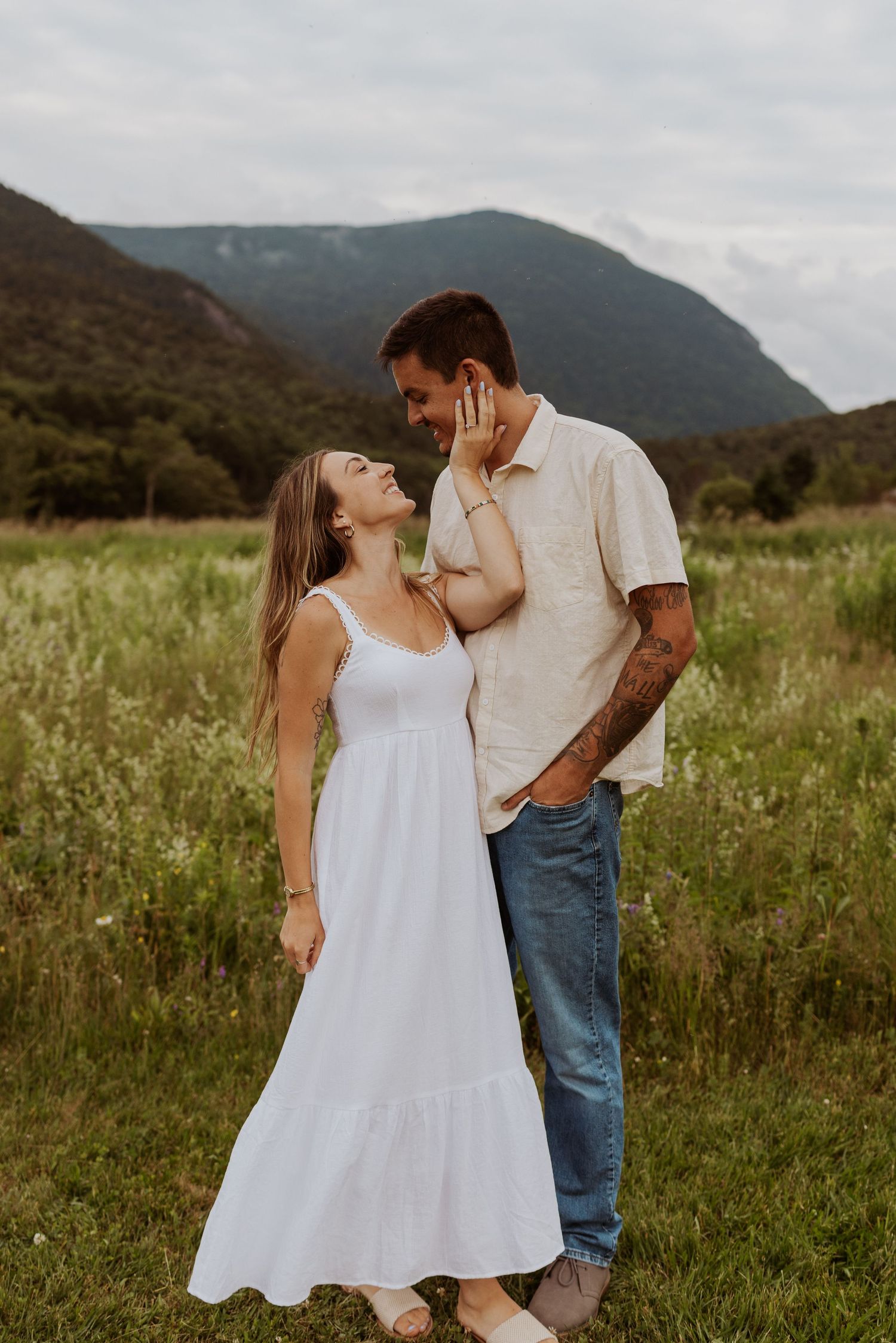Couple gazing at each other lovingly in green meadow with dramatic mountain scenery behind them.